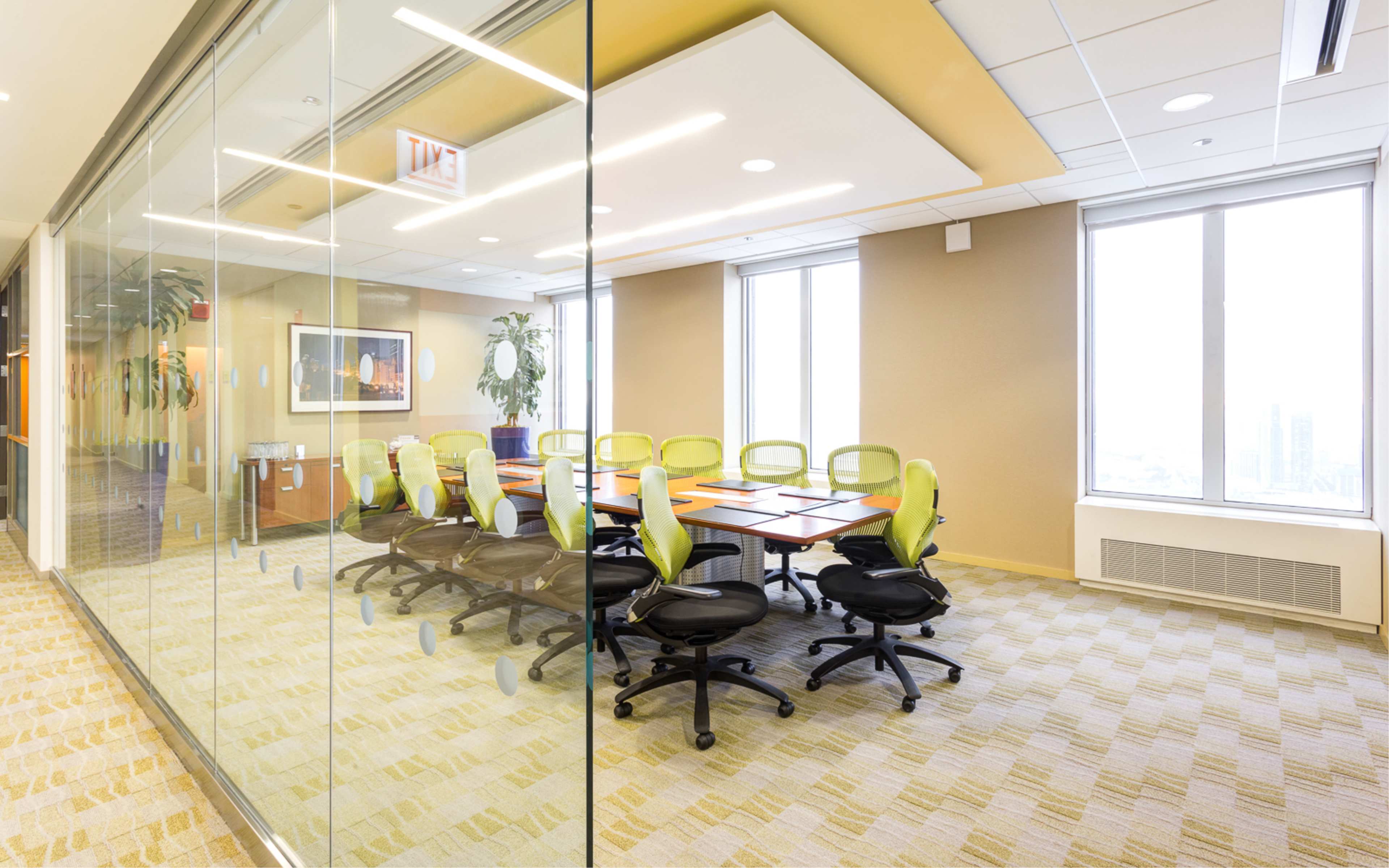 A modern conference room features a long table surrounded by ergonomic green chairs, with large windows providing natural light.