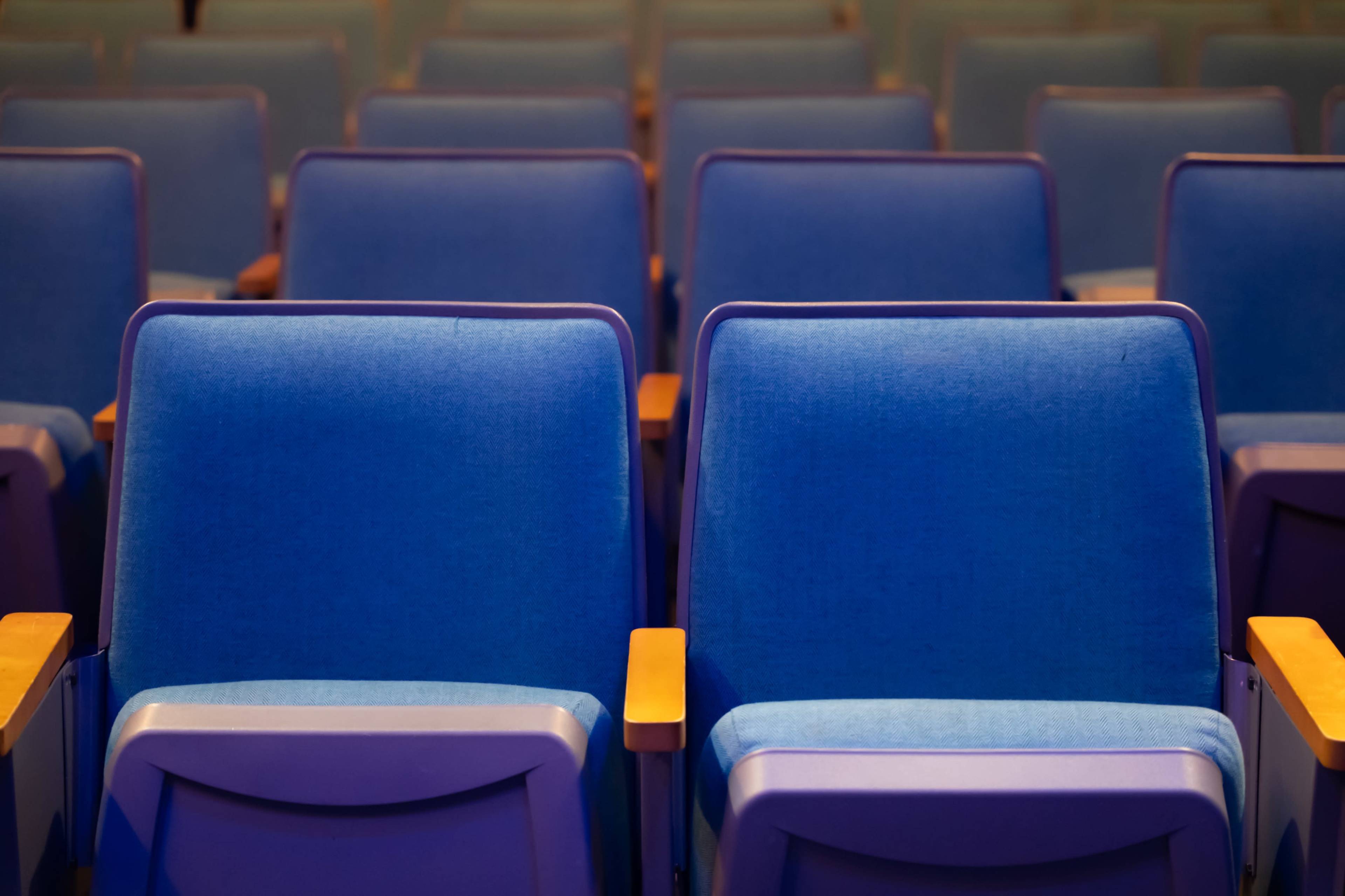 The image shows a series of blue theater seats arranged in rows with wooden armrests.