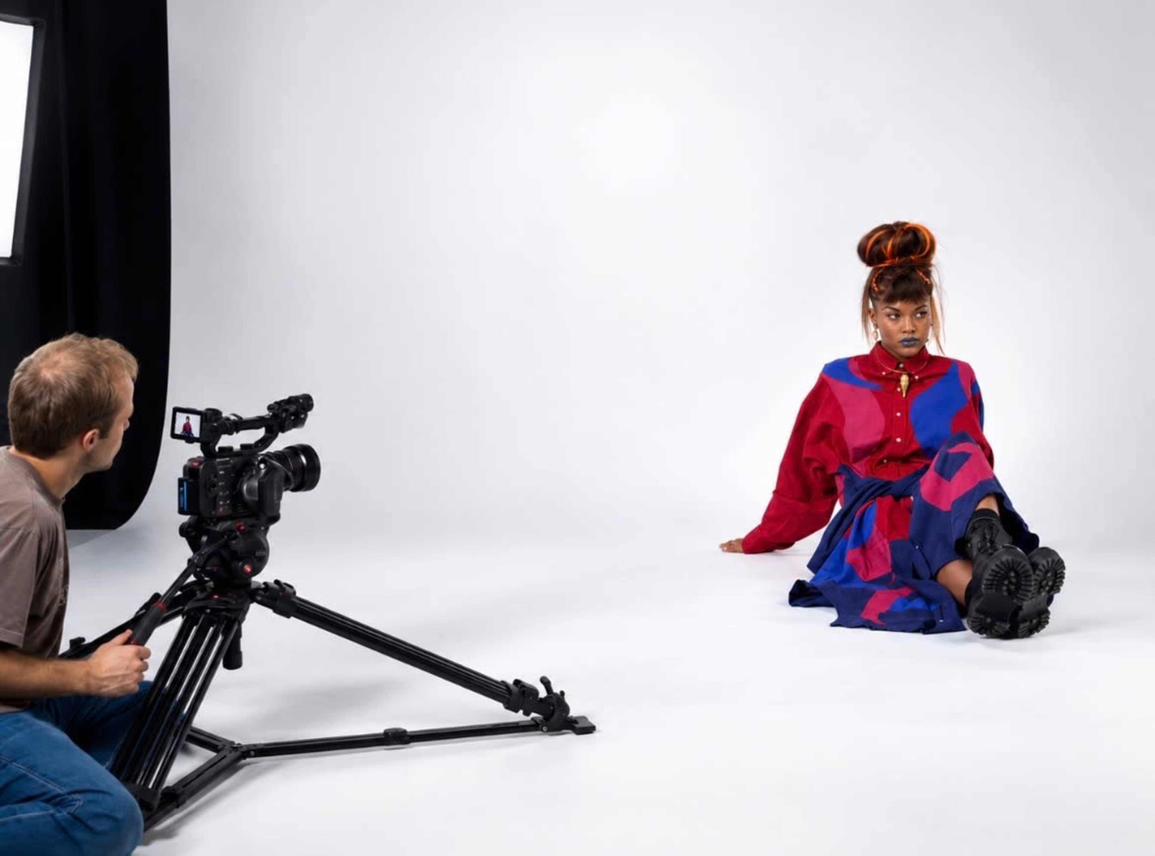 A photographer captures a model posing in a brightly colored outfit against a plain backdrop.