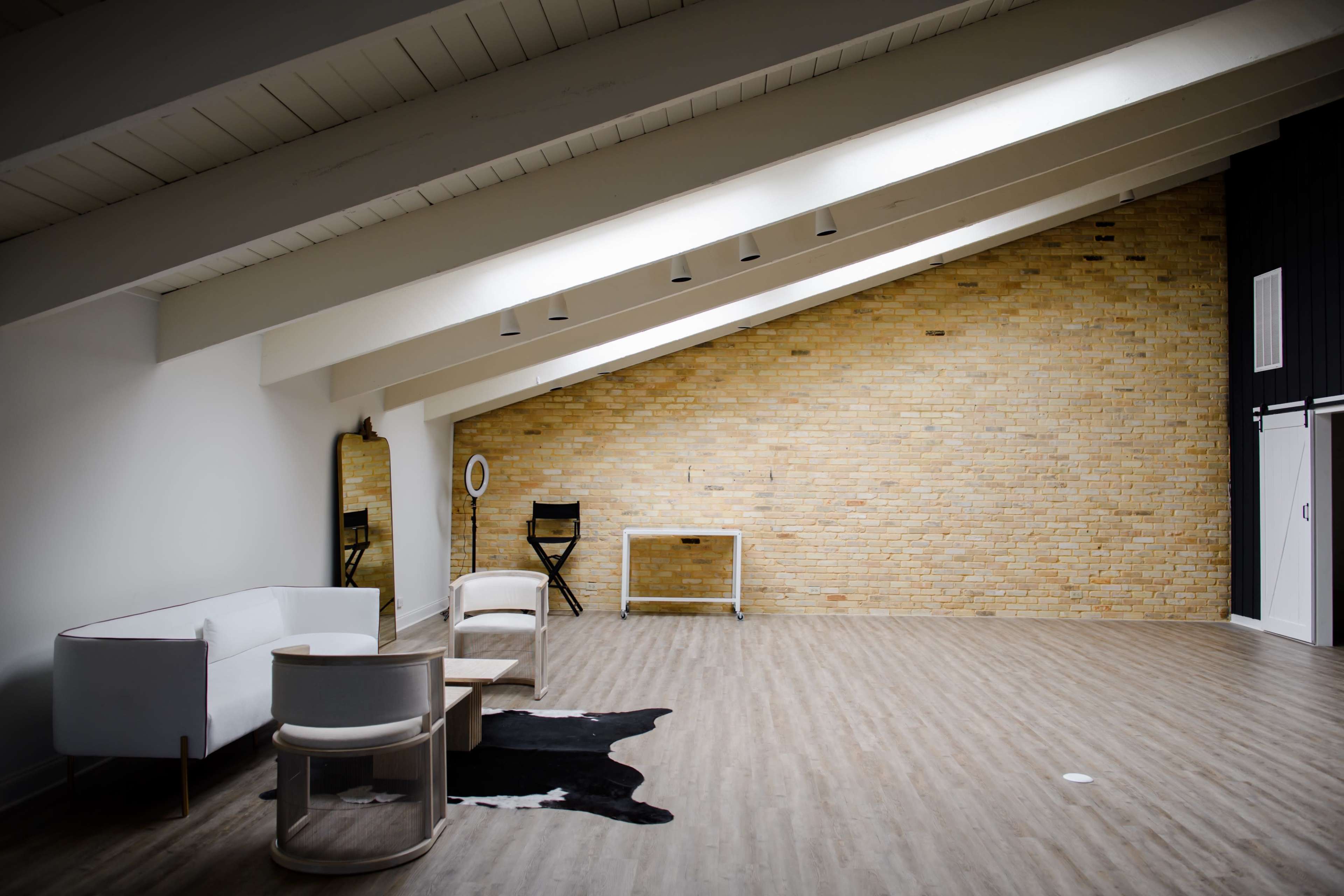 A spacious room with a brick wall, large windows, wooden beams, and minimal furniture, including a white couch and a coffee table.