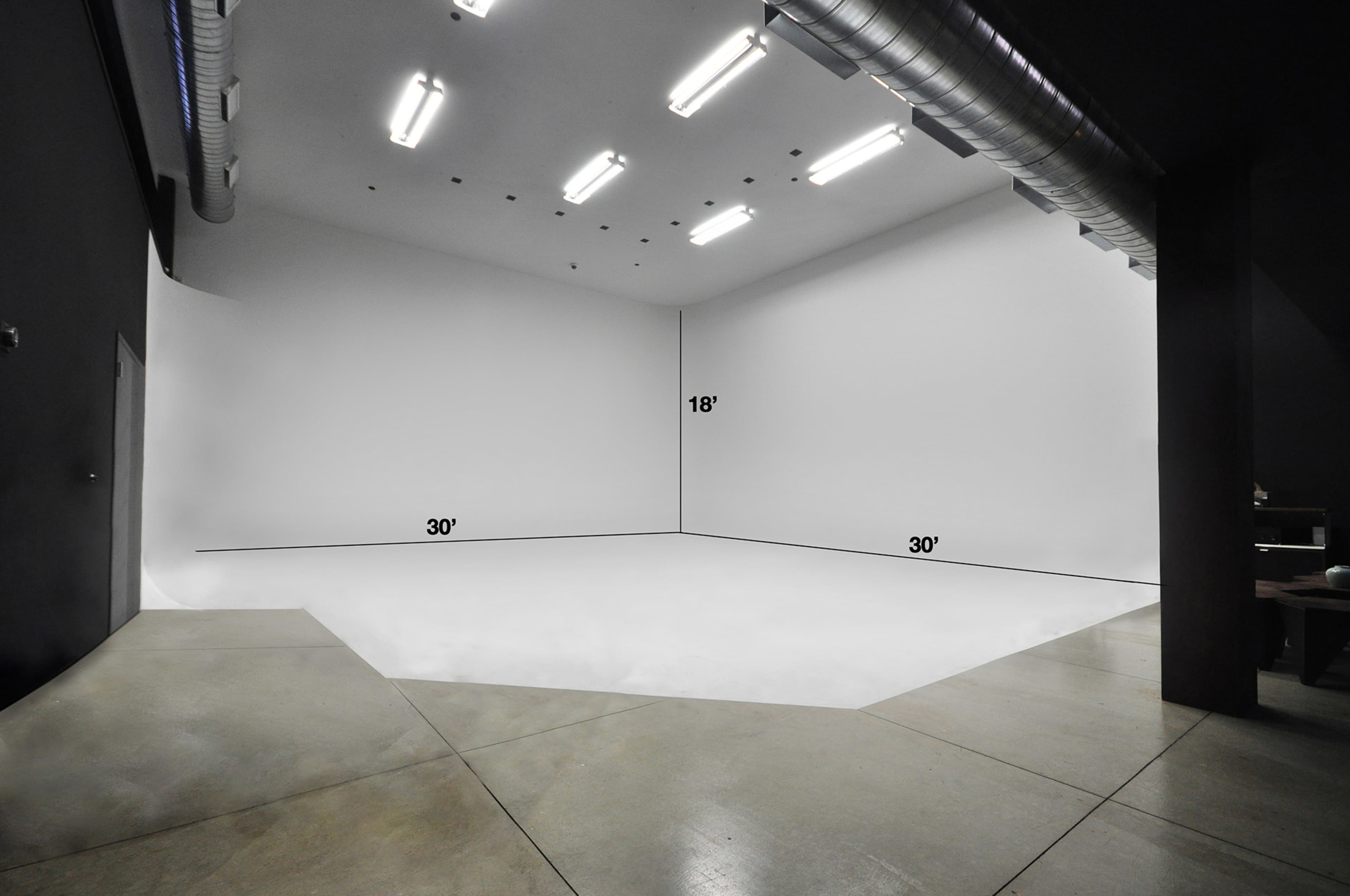 A spacious, empty studio with white walls and a seamless floor, measuring 18 feet by 30 feet on two sides.