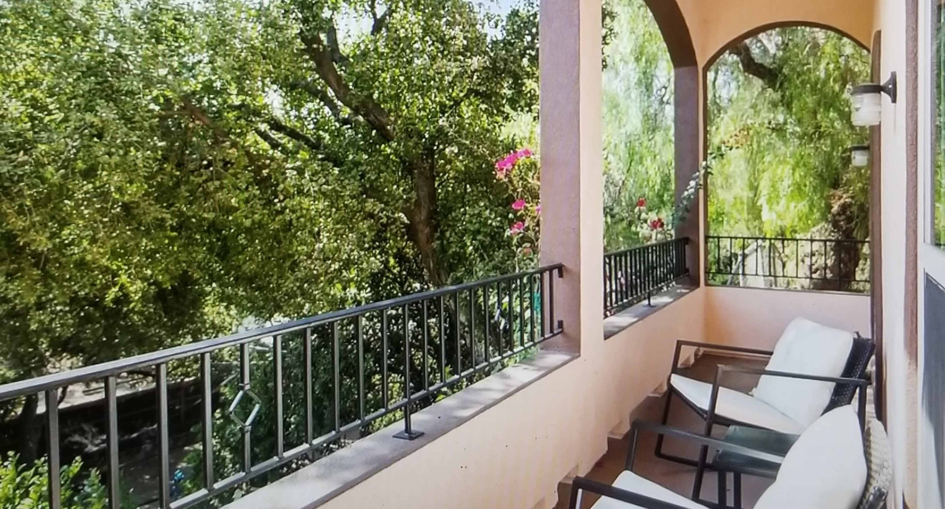 A balcony with black metal chairs overlooks lush greenery and flowering plants.