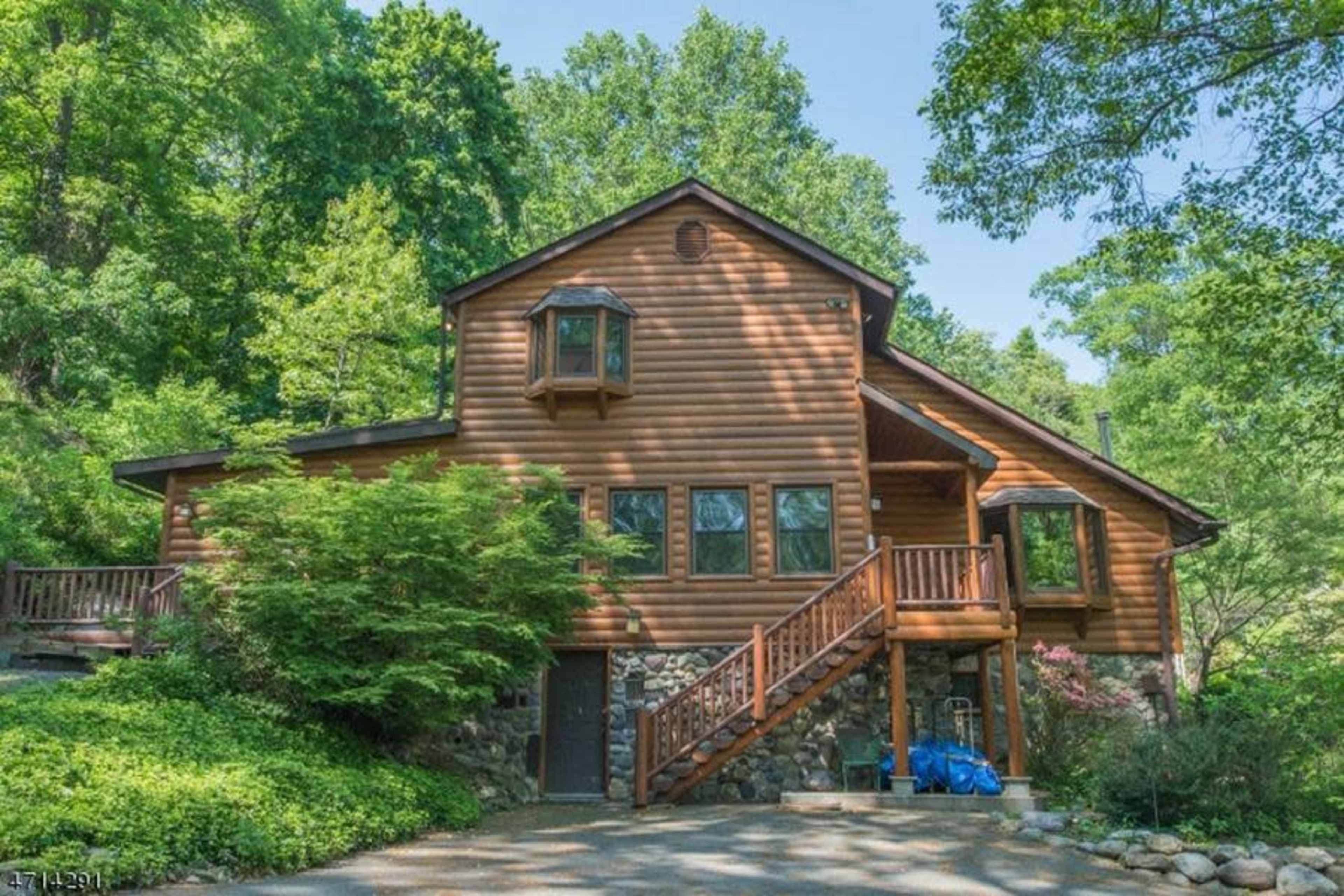 A wooden cabin with large windows and a stone foundation is set amidst lush greenery.