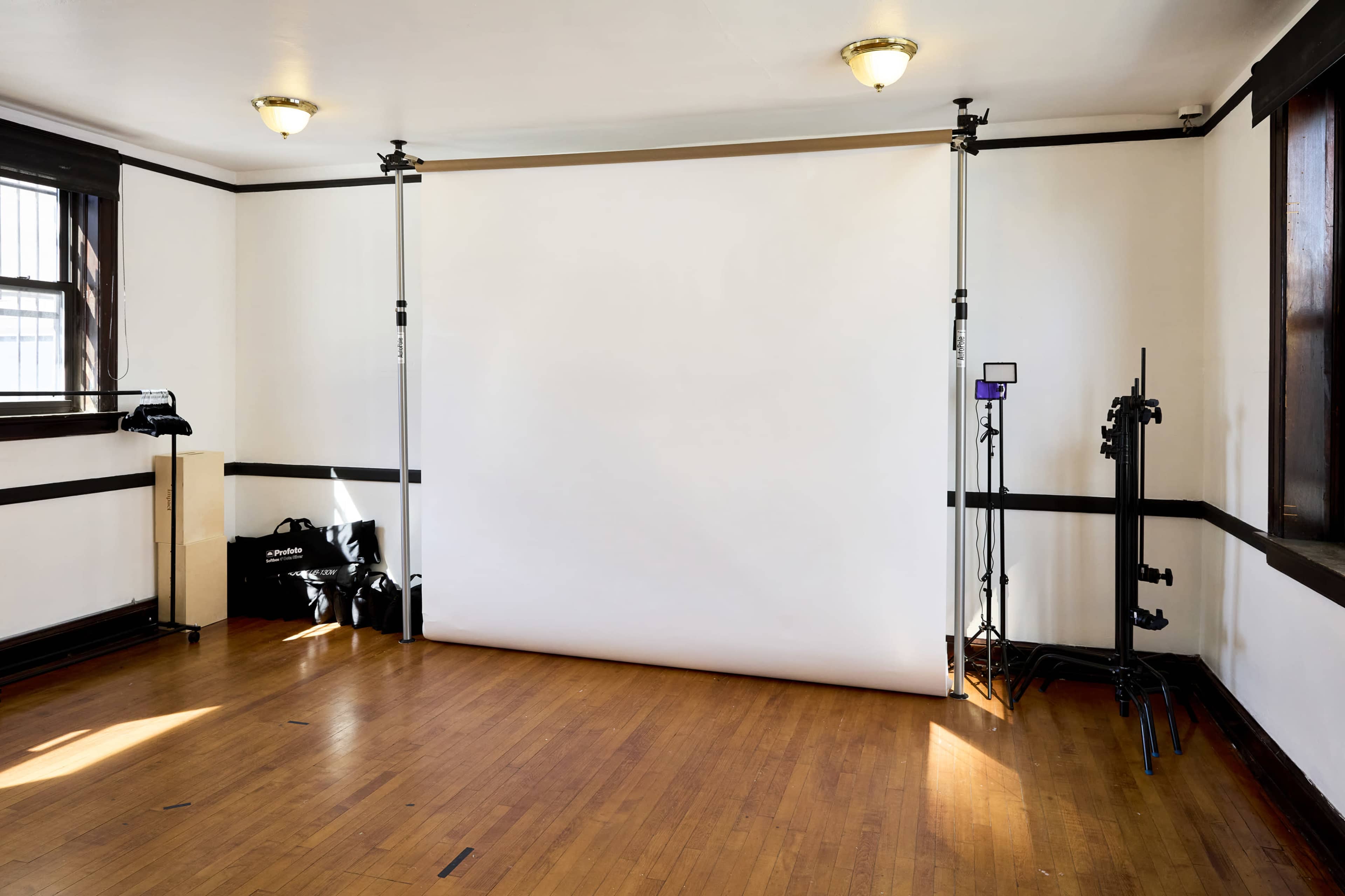 The image shows a photography studio with a white backdrop, lighting equipment, and wooden flooring.