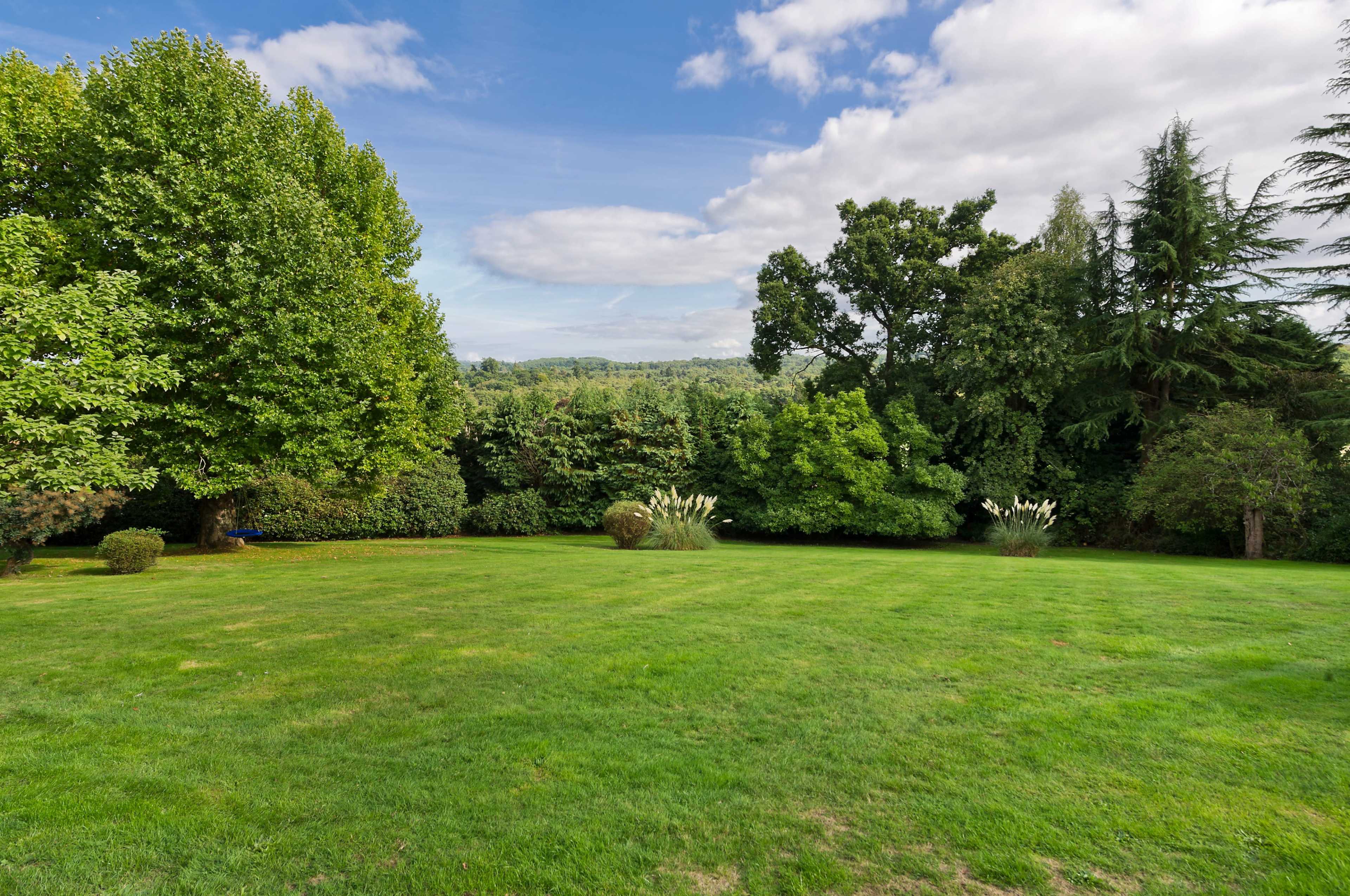 A spacious green lawn bordered by trees and shrubs under a partly cloudy sky.