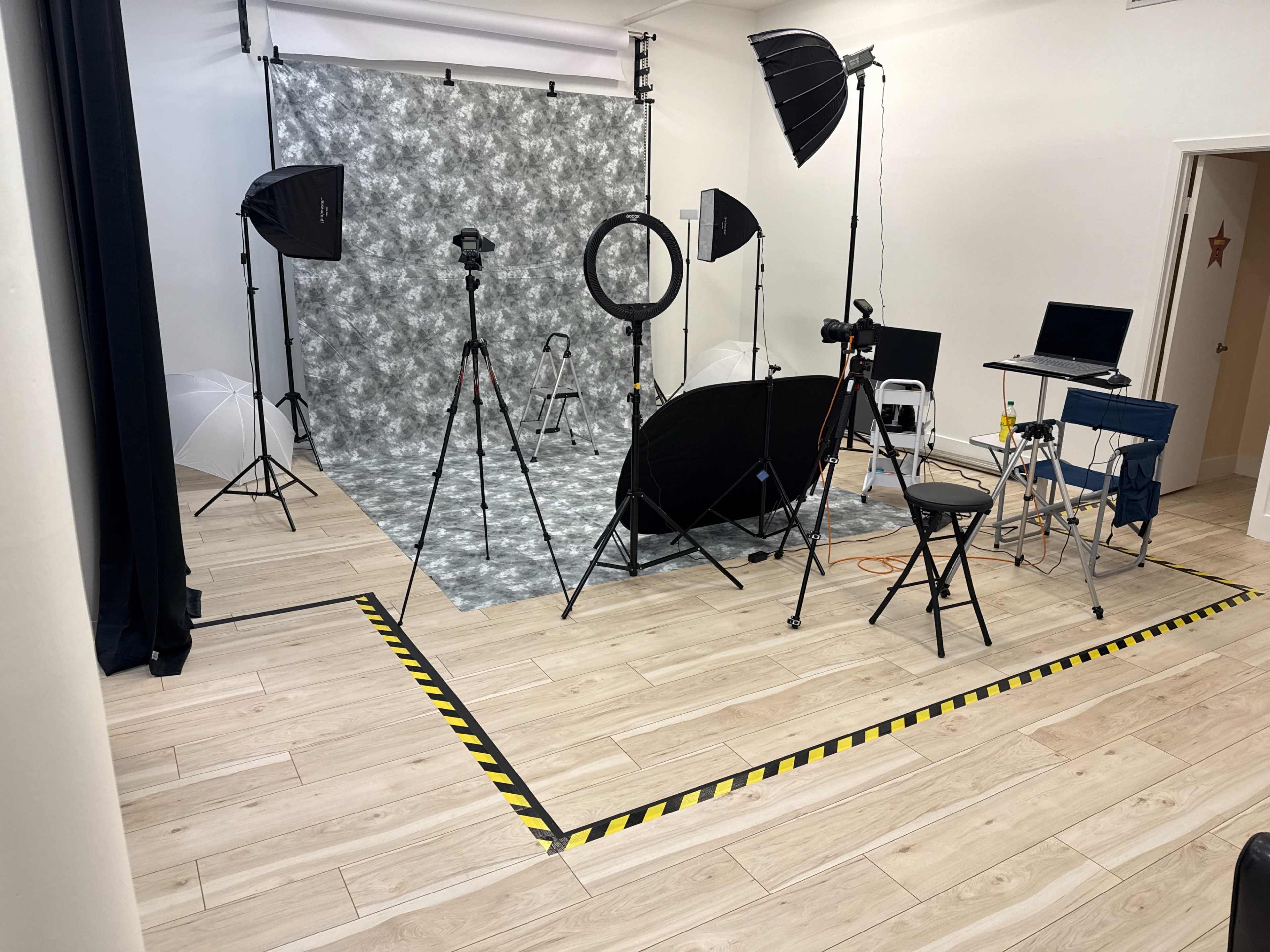 The image shows a photography studio setup with various lighting equipment, backdrops, and cameras arranged on a wooden floor.