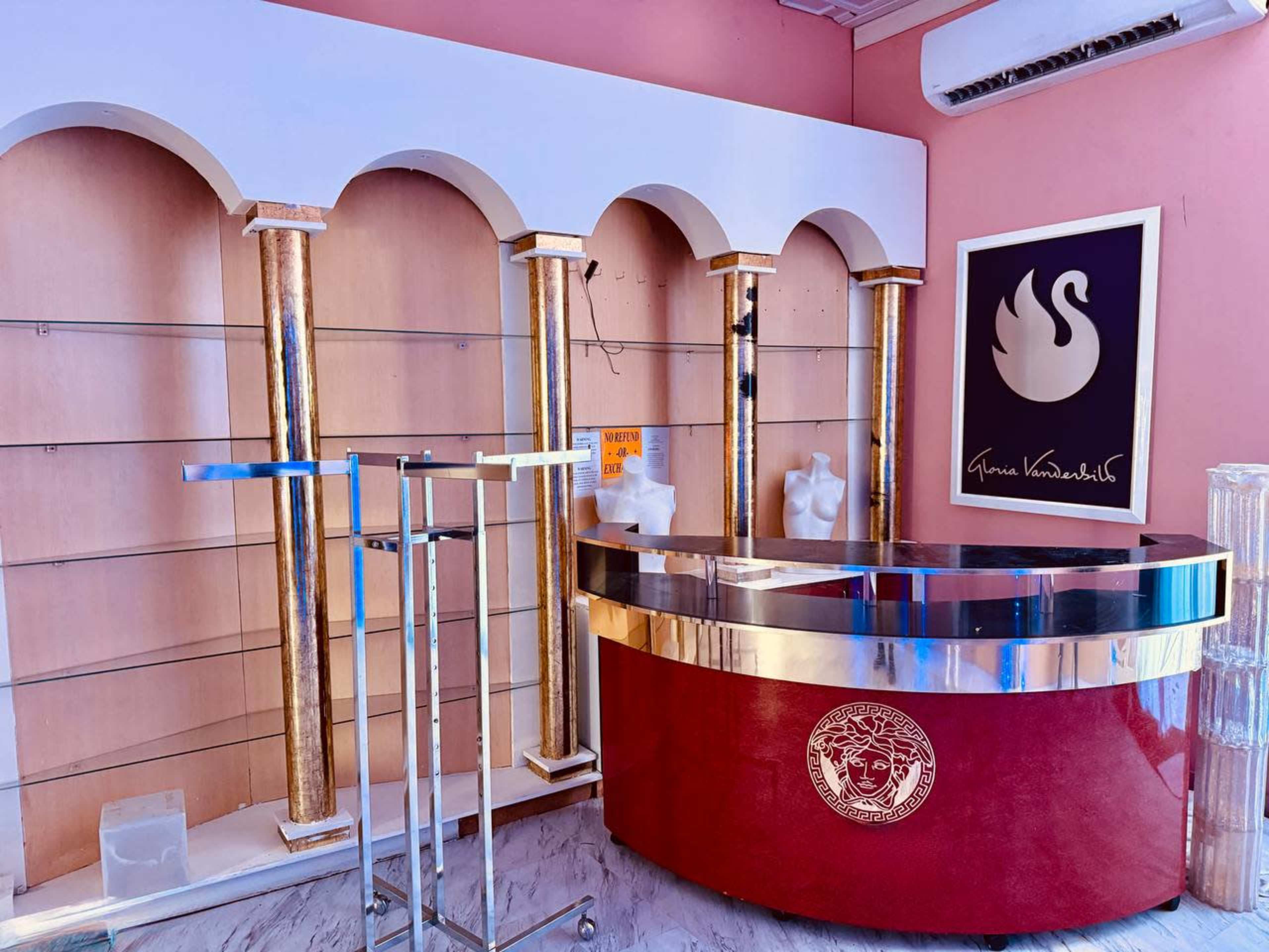 The image shows a store interior featuring a red counter with silver trim and golden columns, alongside empty shelves and a framed artwork on the wall.