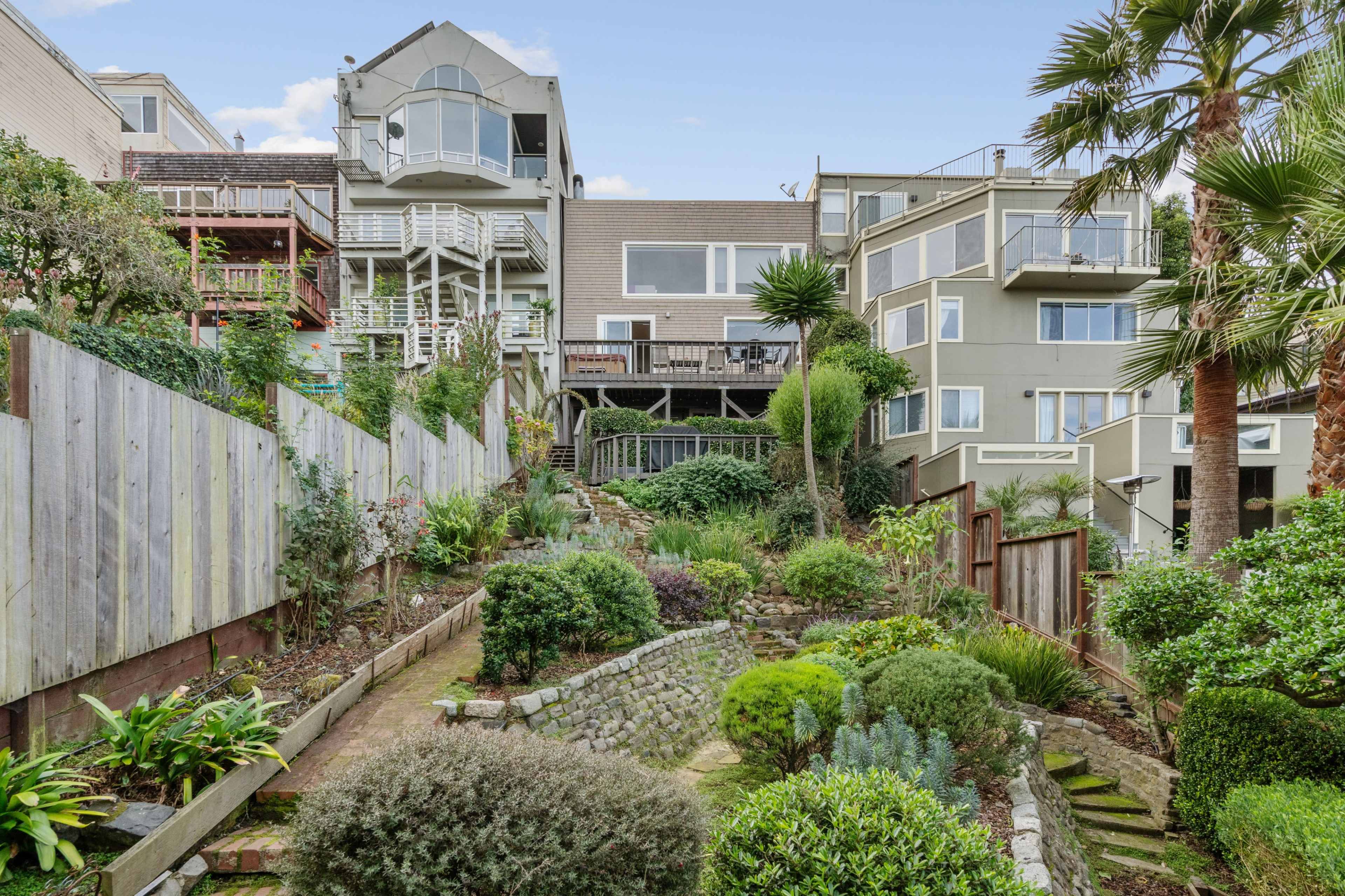 The image shows a landscaped garden with a terraced design, leading up to multiple modern buildings.
