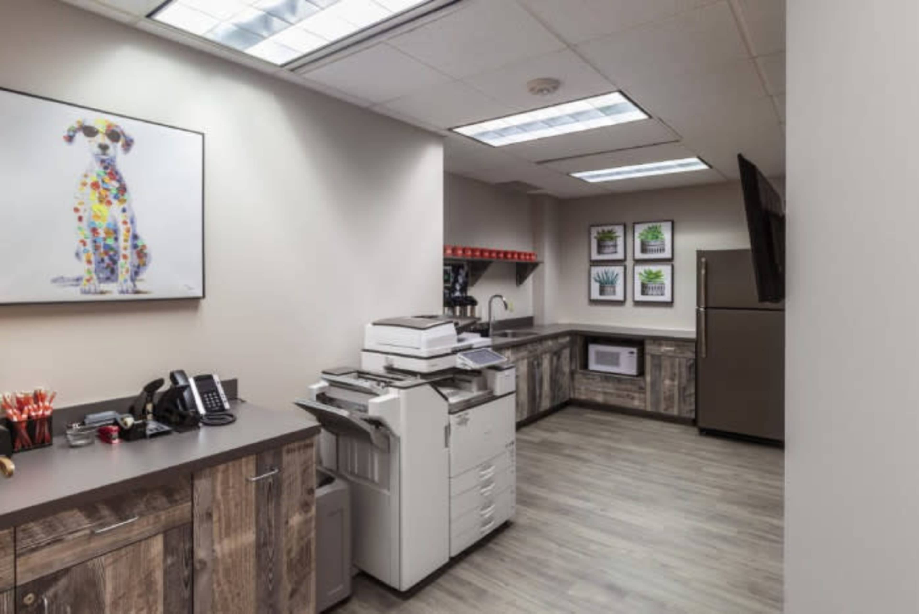 An office break room featuring a copier, a refrigerator, a microwave, and framed artwork on the walls.