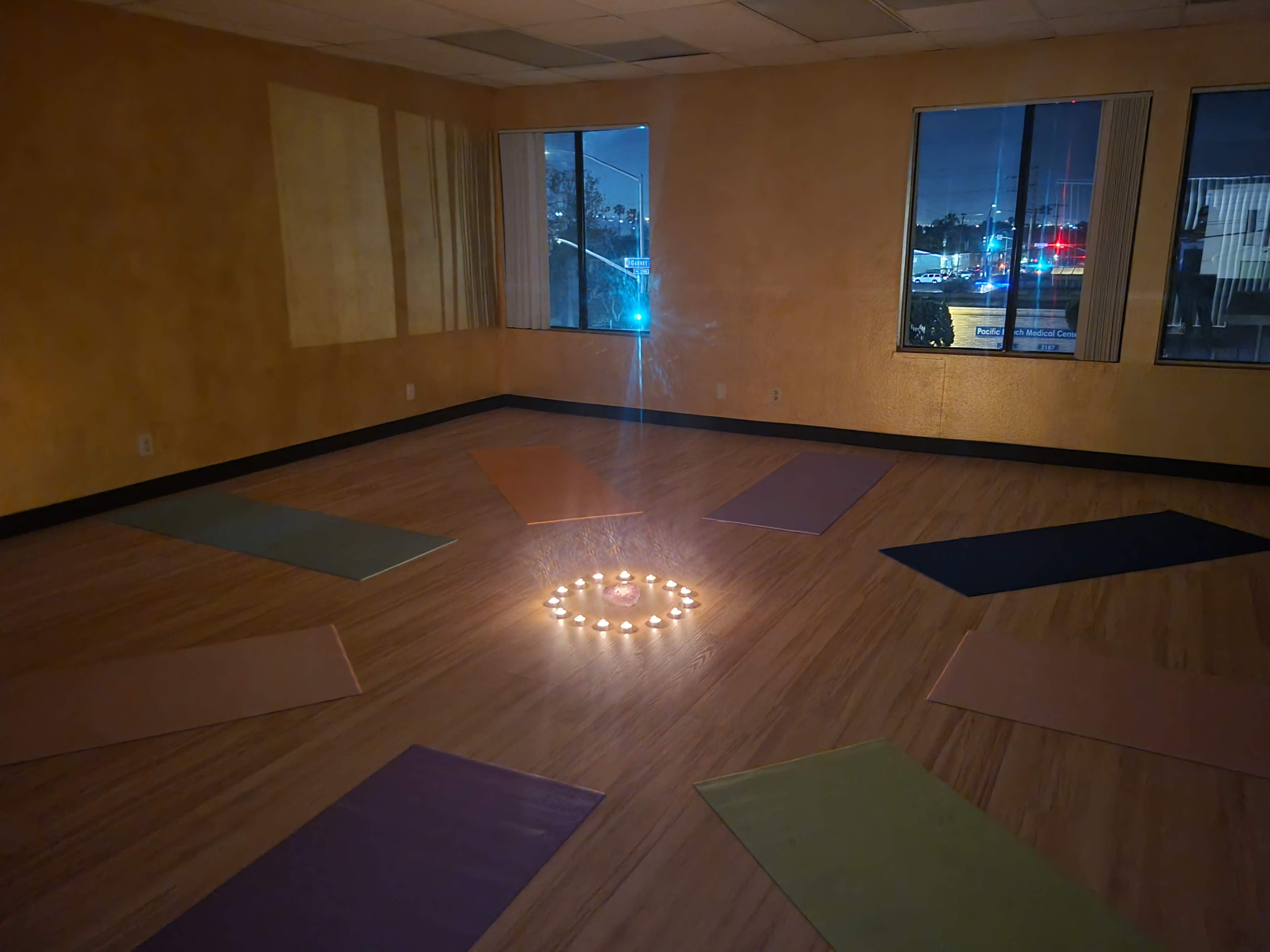 A yoga studio features several mats arranged in a circle around a candle display in a dimly lit space.