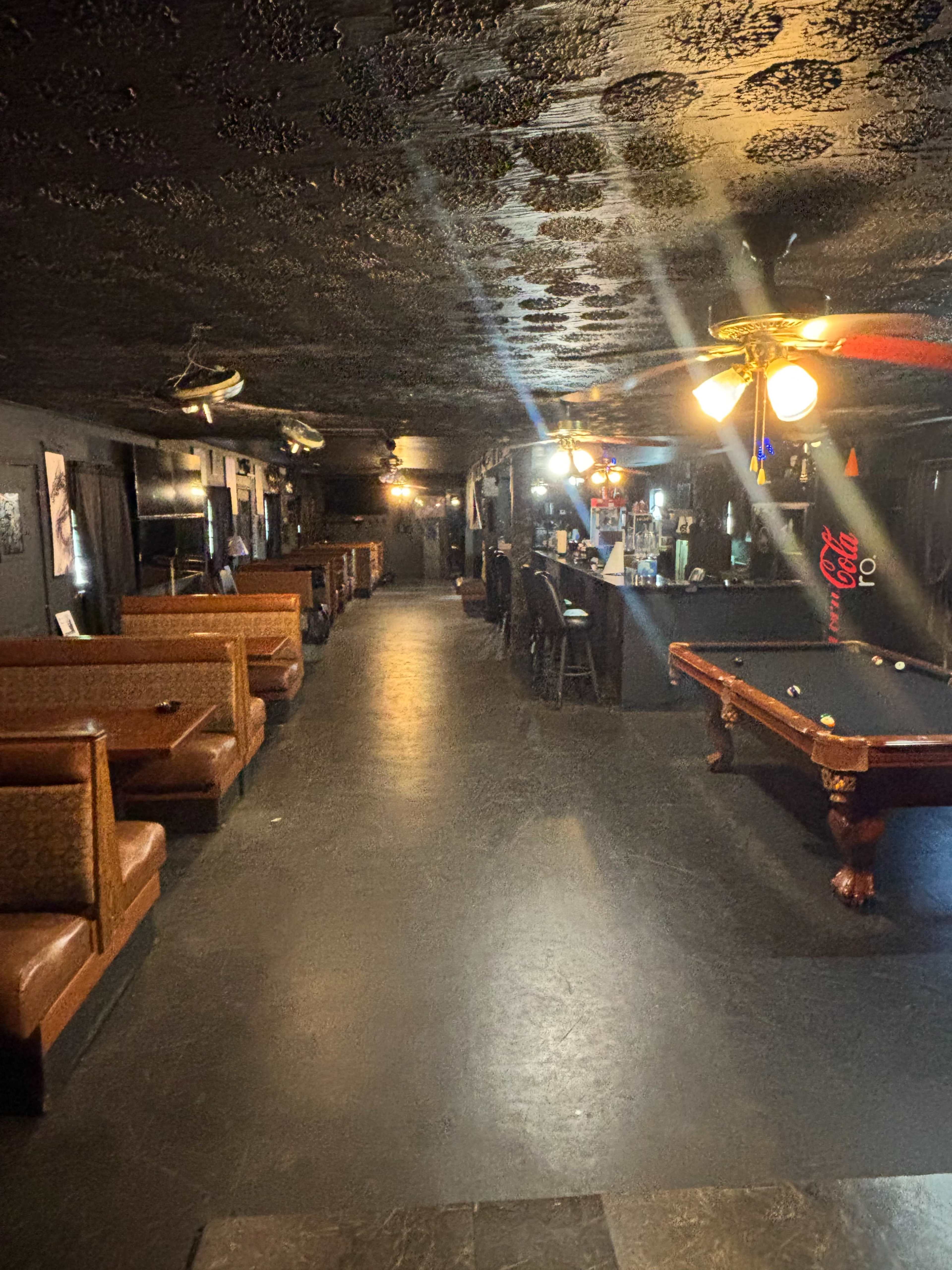 The image shows a dimly lit bar interior with seating booths along one side and a pool table near the center.