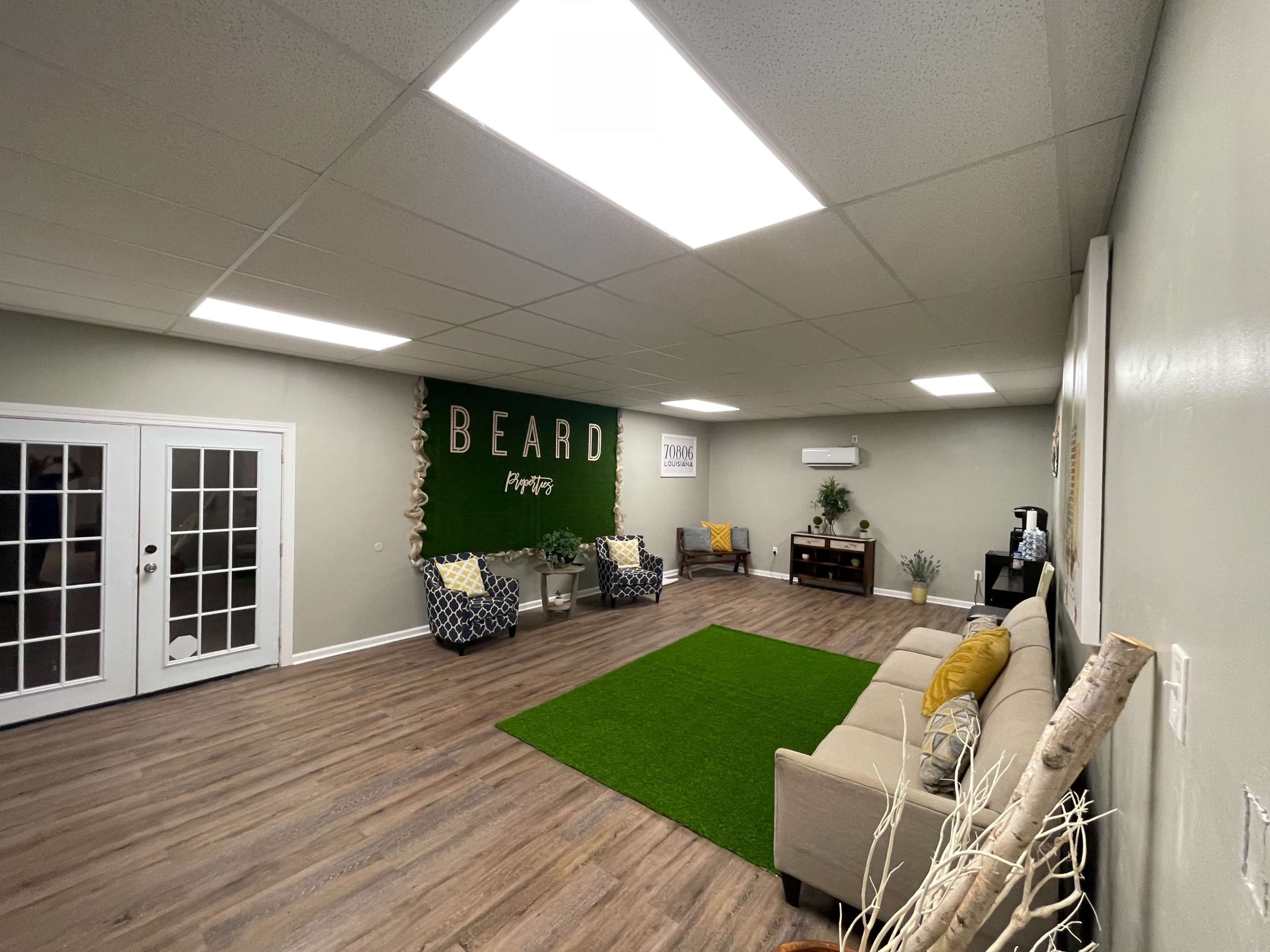 The room features a green carpet area, light-colored couches, and a wall with the word "BEARD" prominently displayed, along with two seating areas.