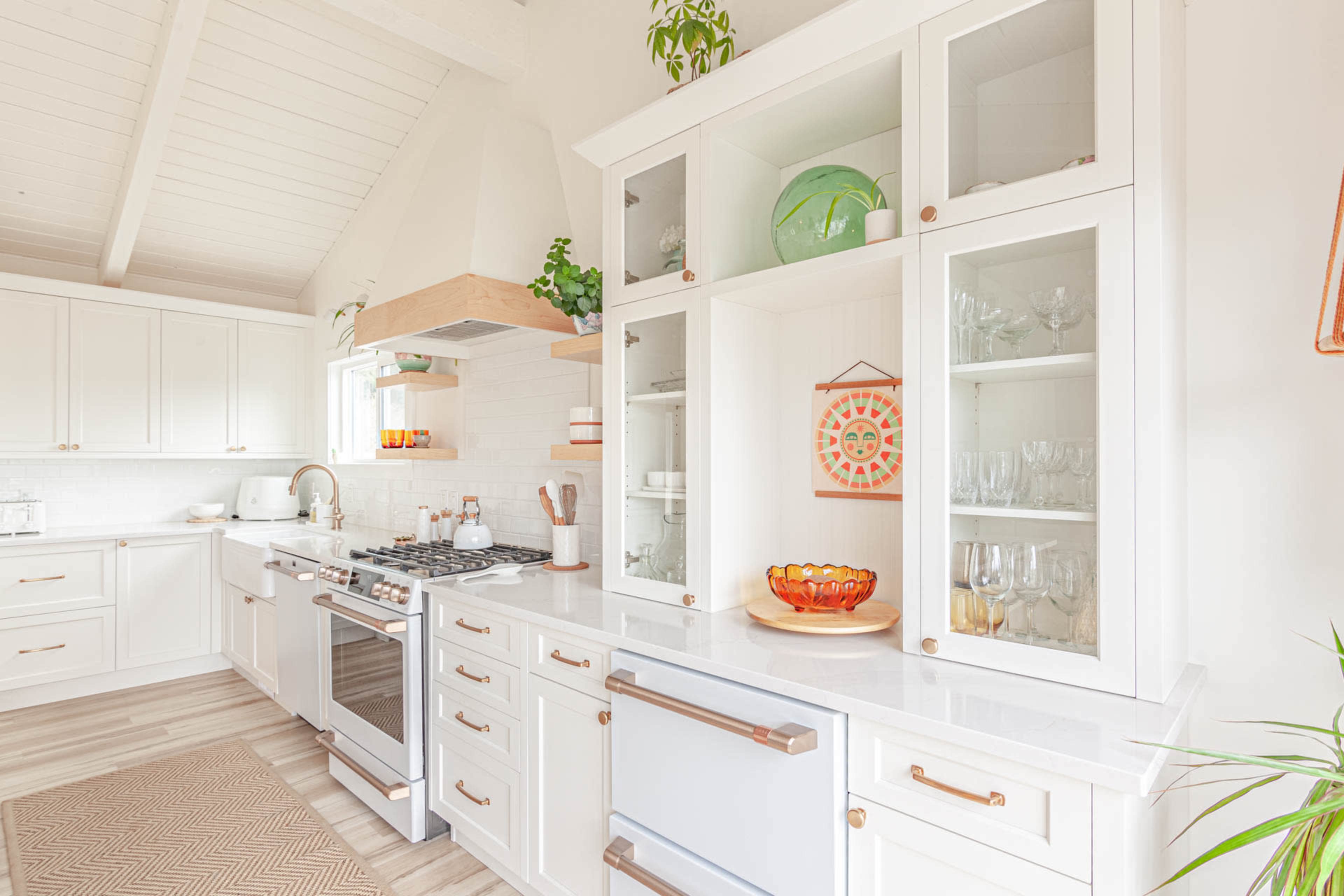 A modern kitchen features white cabinetry, stainless steel appliances, and a central island with glass-front cabinets displaying decorative items.