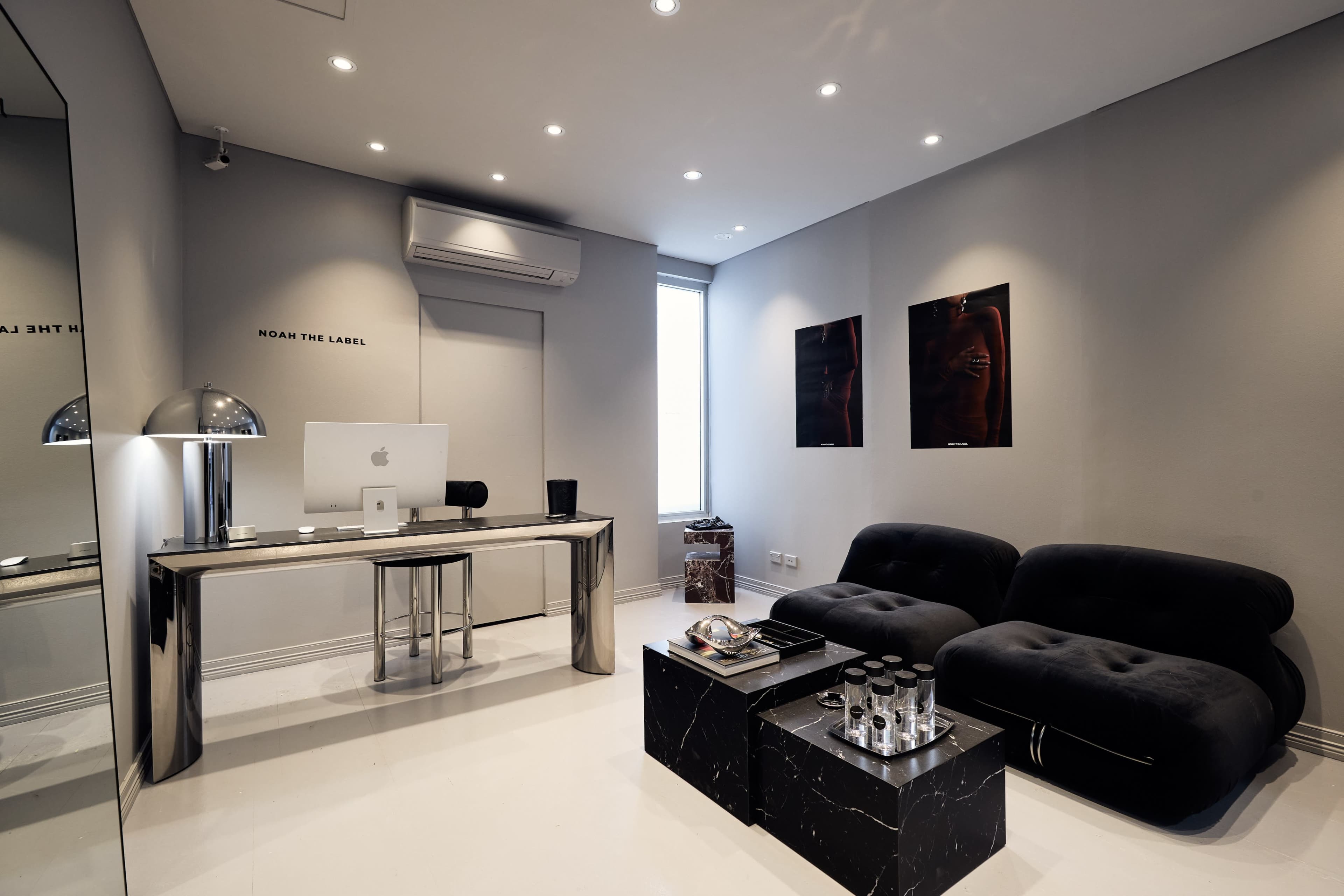 The image shows a modern office space featuring a sleek desk with an iMac, two dark velvet sofas, and minimalist decor on the walls.