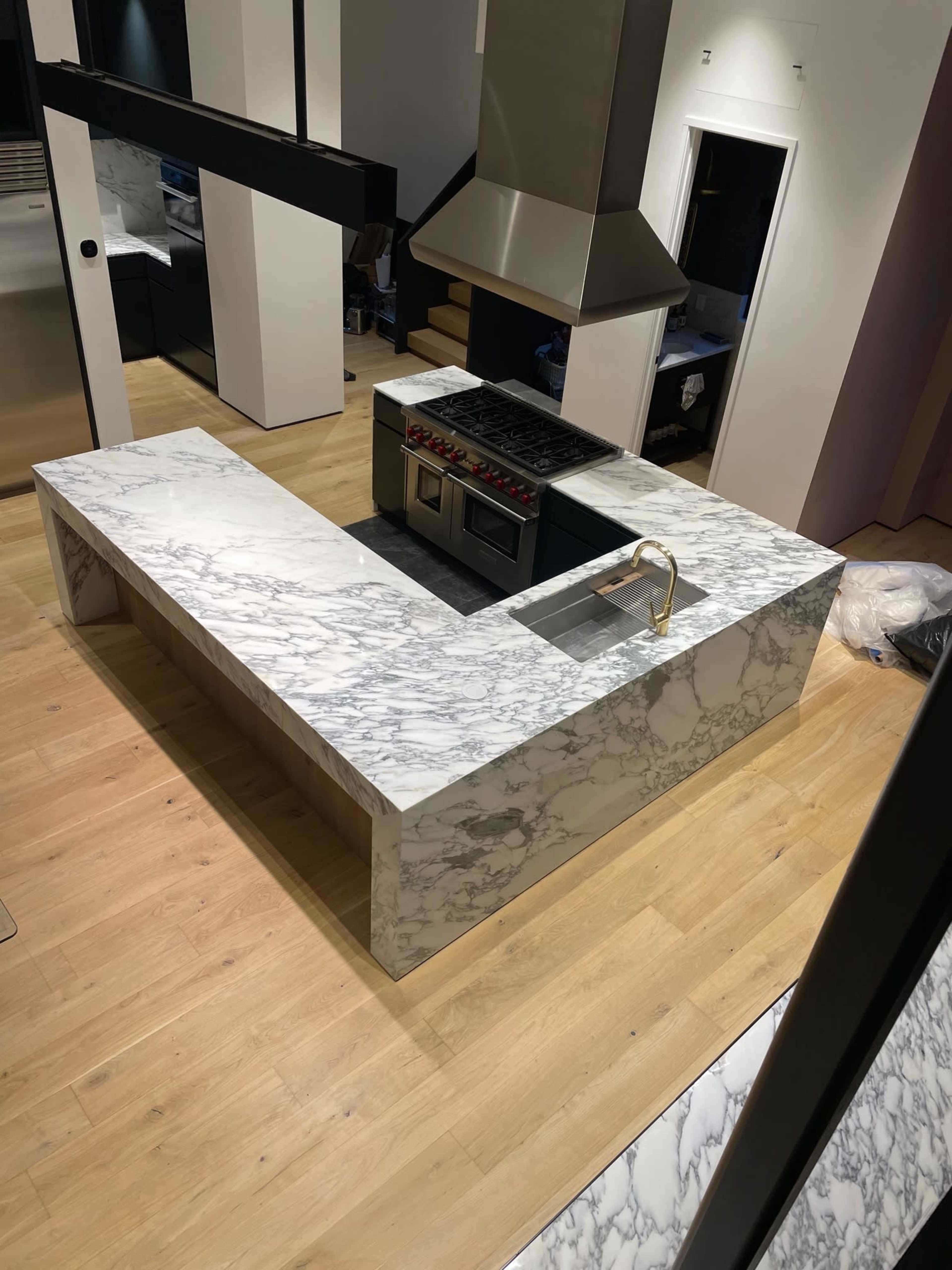 A modern kitchen features a large, L-shaped marble countertop with a built-in sink and stove.