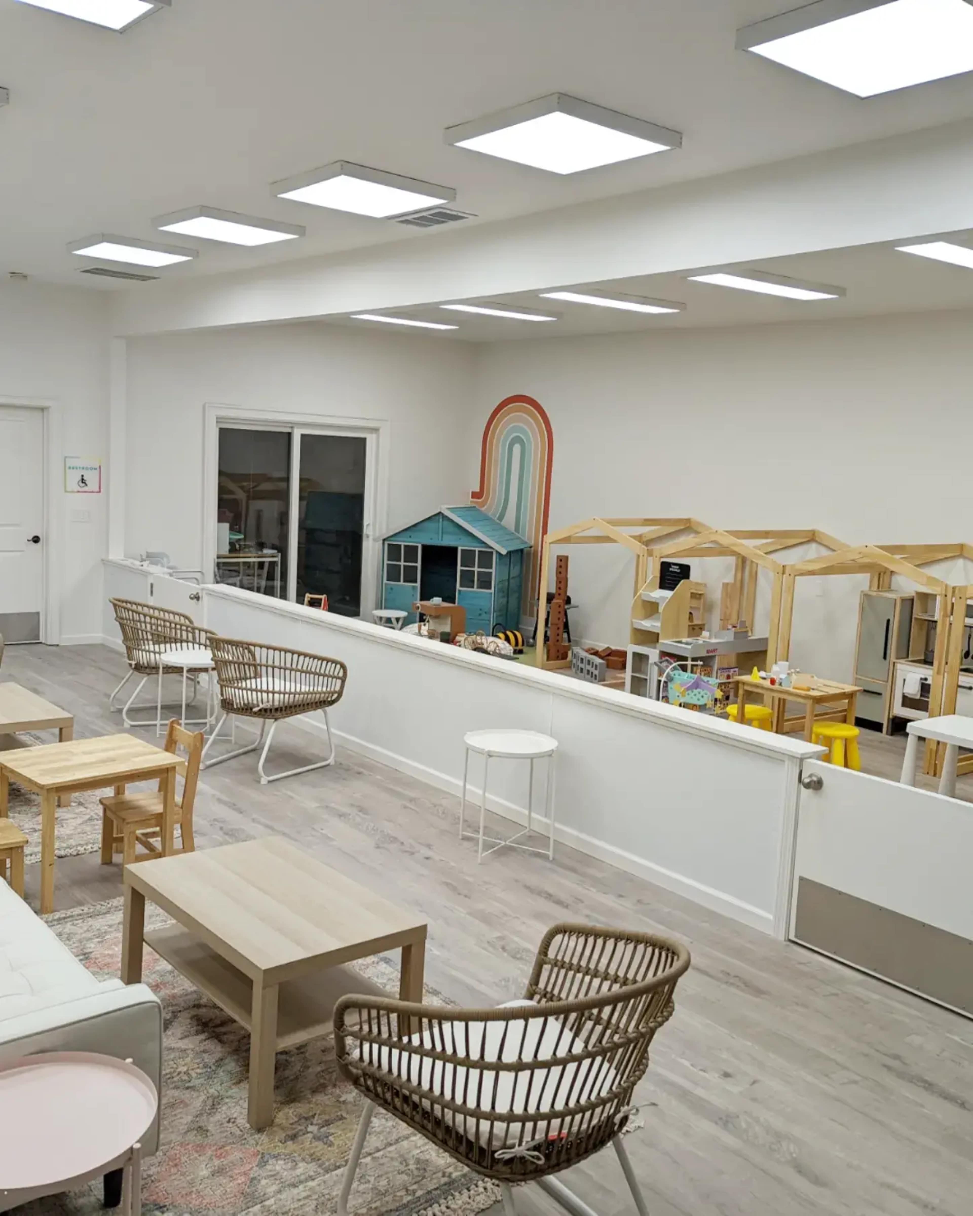 A bright, modern playroom with colorful toys, wooden playhouses, and seating arrangements.