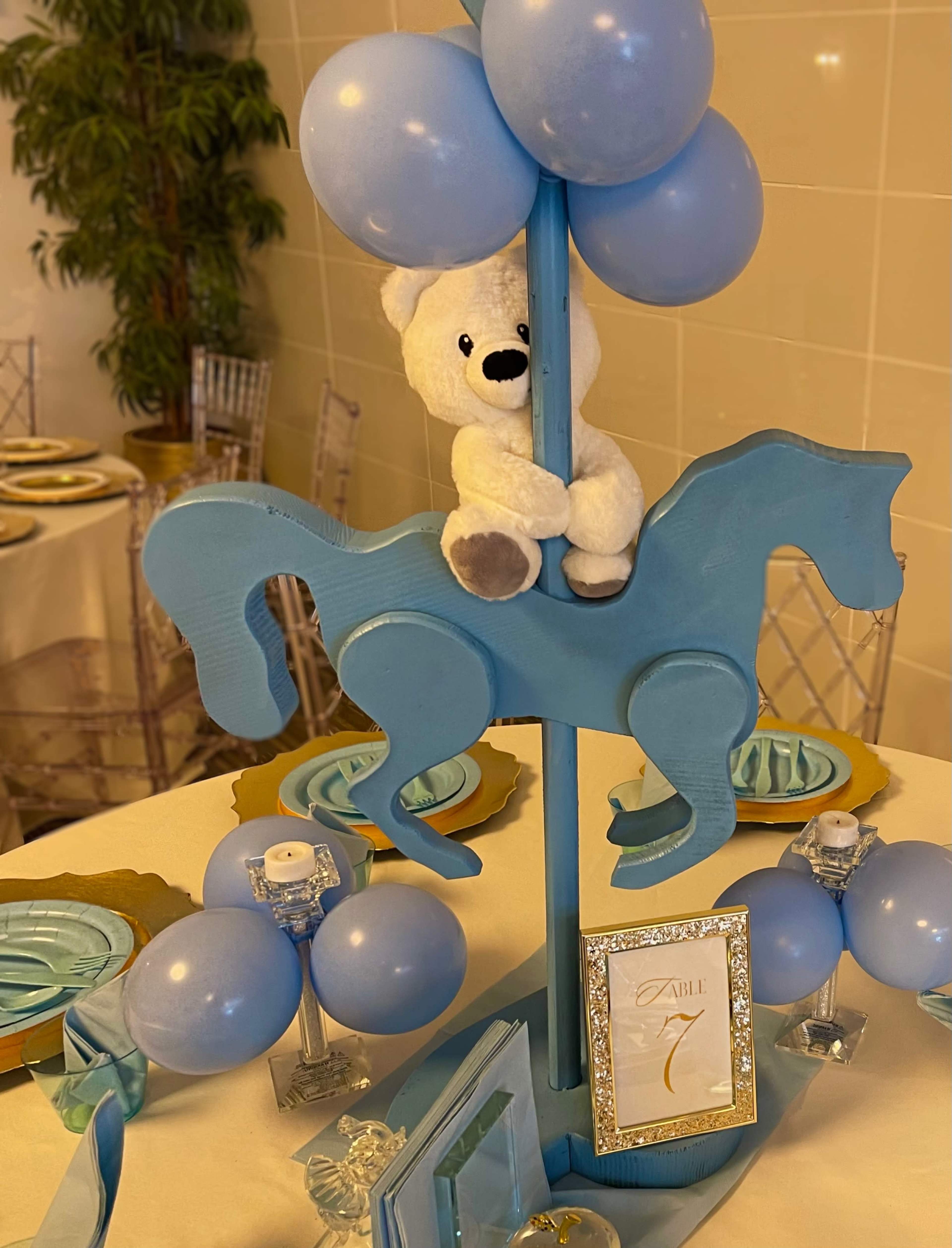 A table centerpiece features a blue horse with a teddy bear perched on top, surrounded by blue balloons and decorative elements.