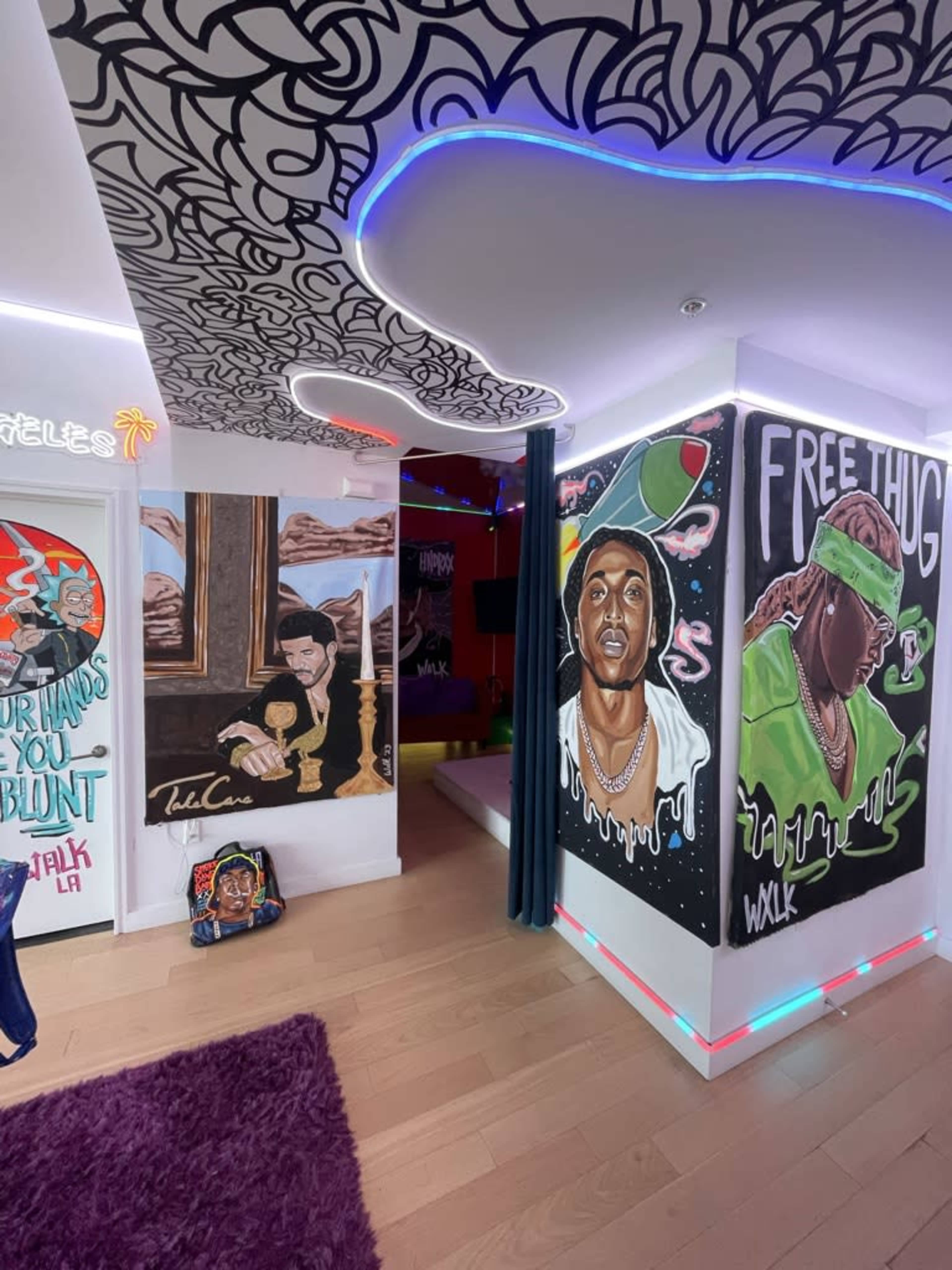 The image shows a colorful room featuring artistic wall murals, including portraits and graffiti, with modern lighting and a plush rug underfoot.