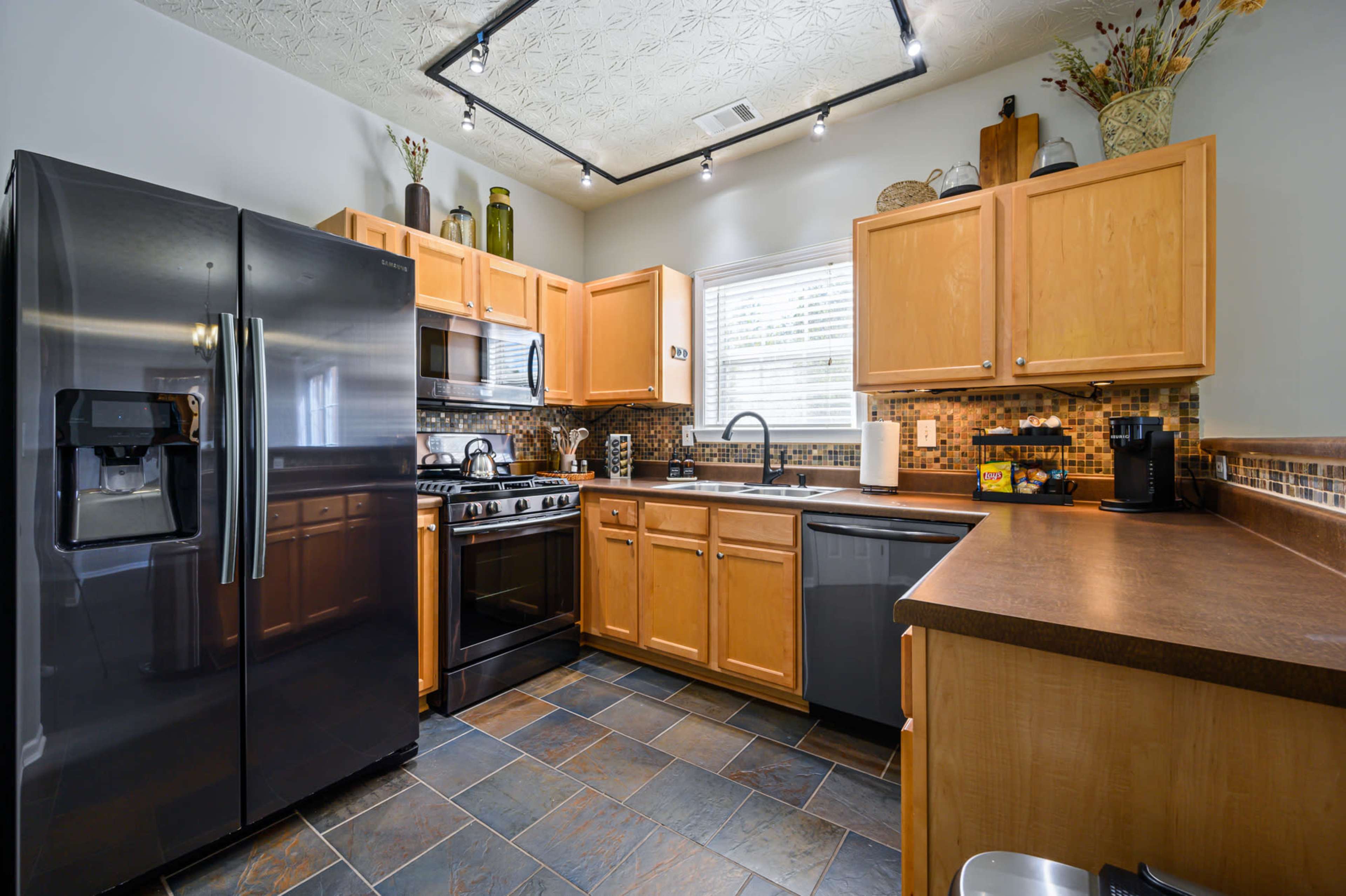 A modern kitchen with wooden cabinets, stainless steel appliances, and a slate tile floor.