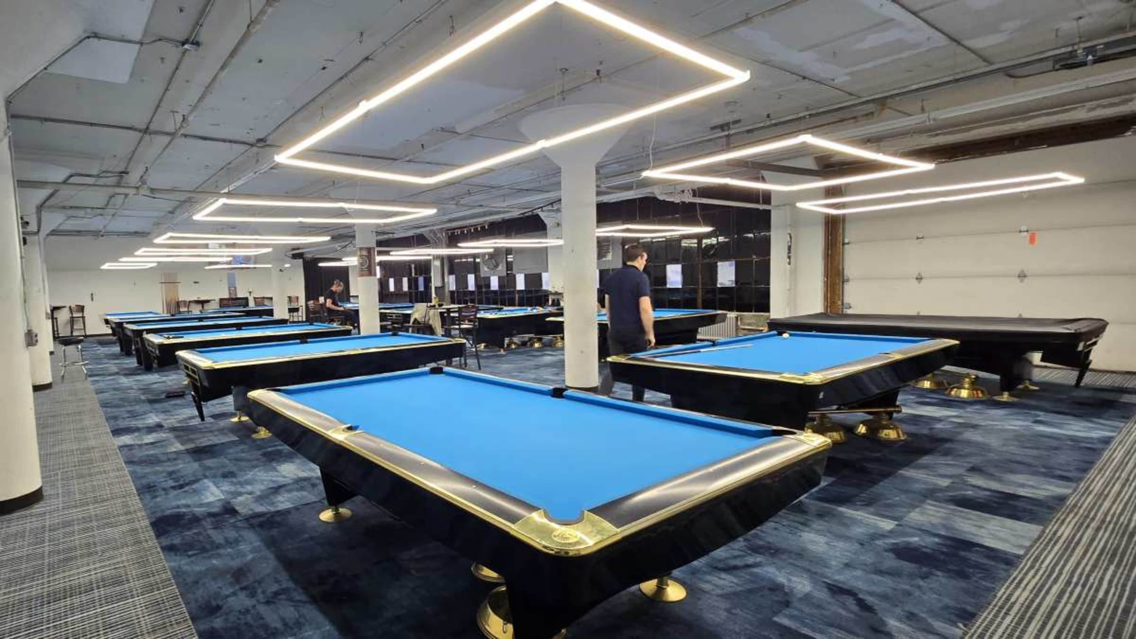 The image shows a spacious billiards room featuring several pool tables arranged neatly under modern lighting.
