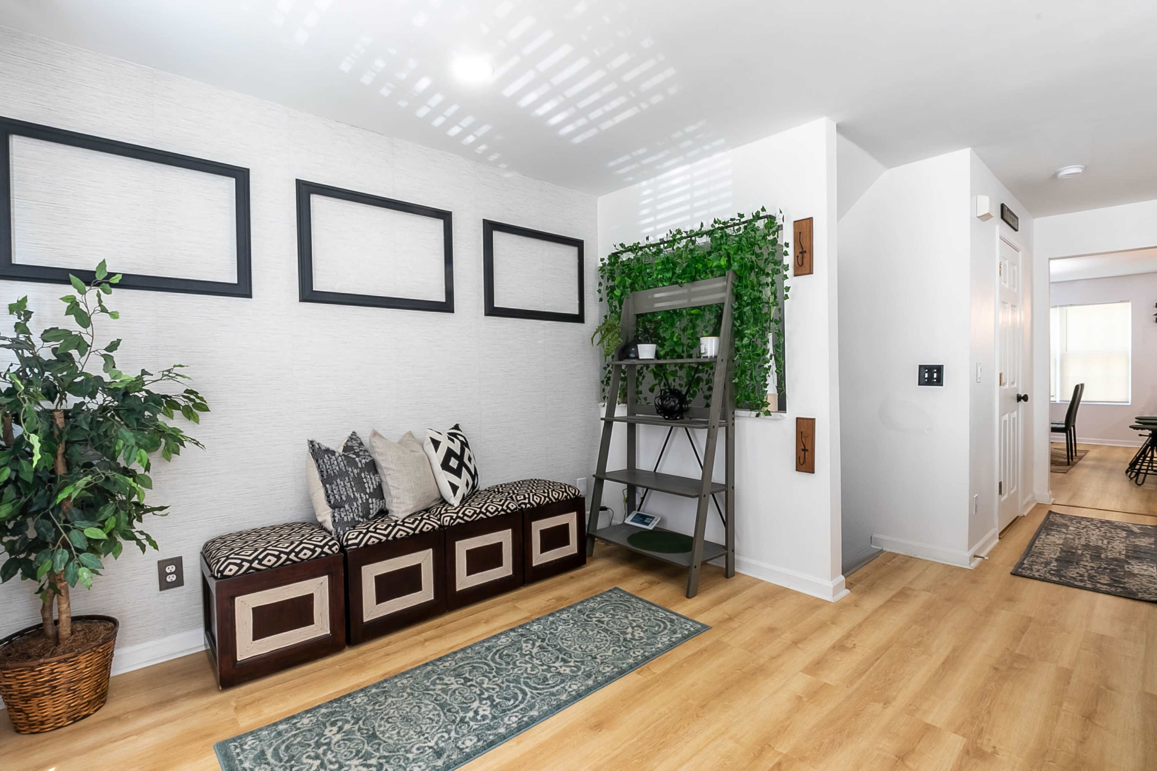 A modern entryway with a bench, decorative pillows, a plant, and a ladder shelf against a textured wall.