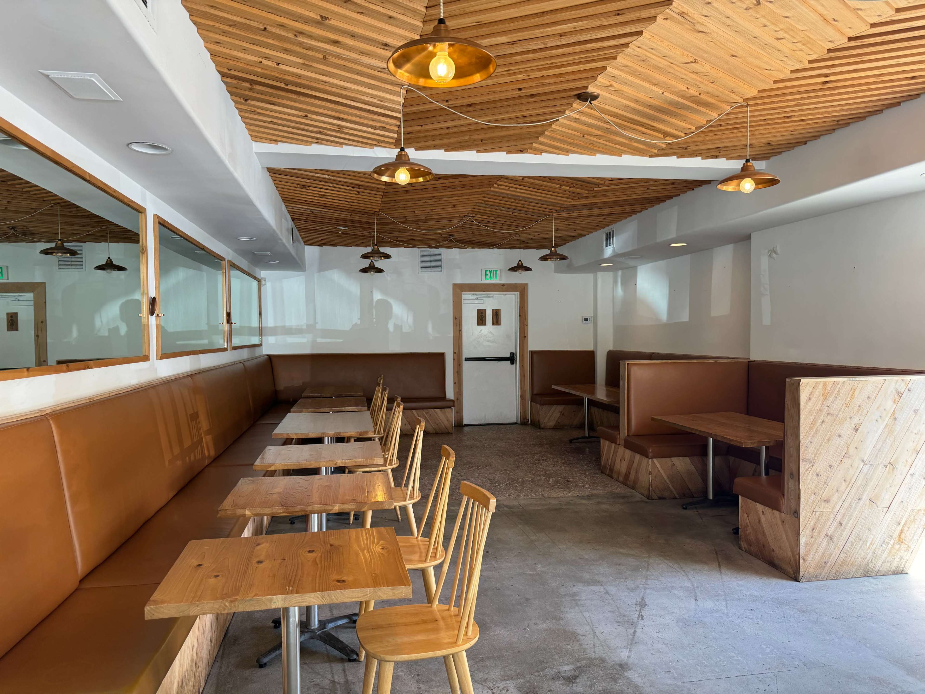 A modern cafe interior featuring wooden paneling, several tables, and a few booths along the walls.