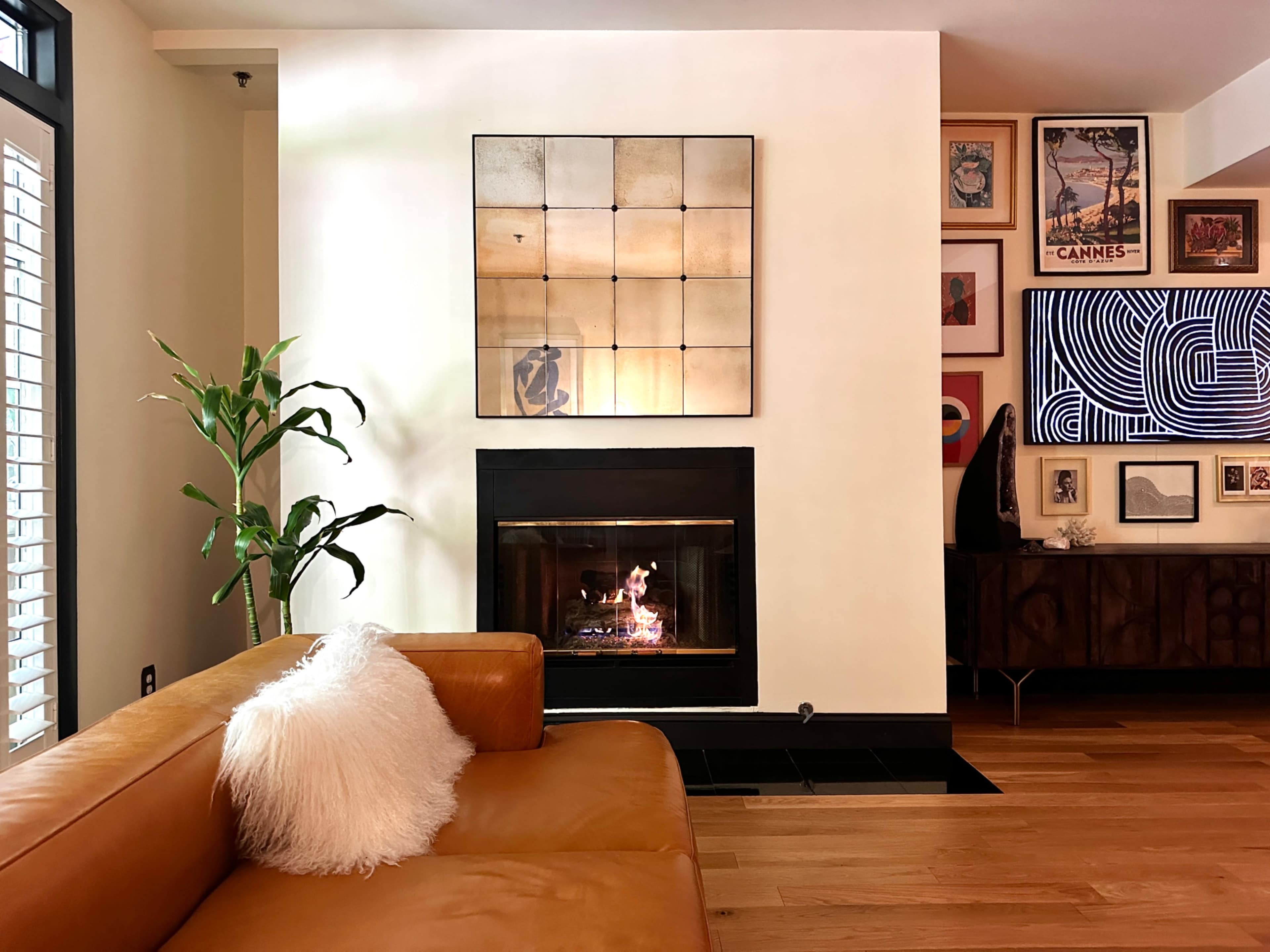 The image shows a modern living room featuring a leather sofa, a fireplace with a fire burning, and artwork displayed on the walls.