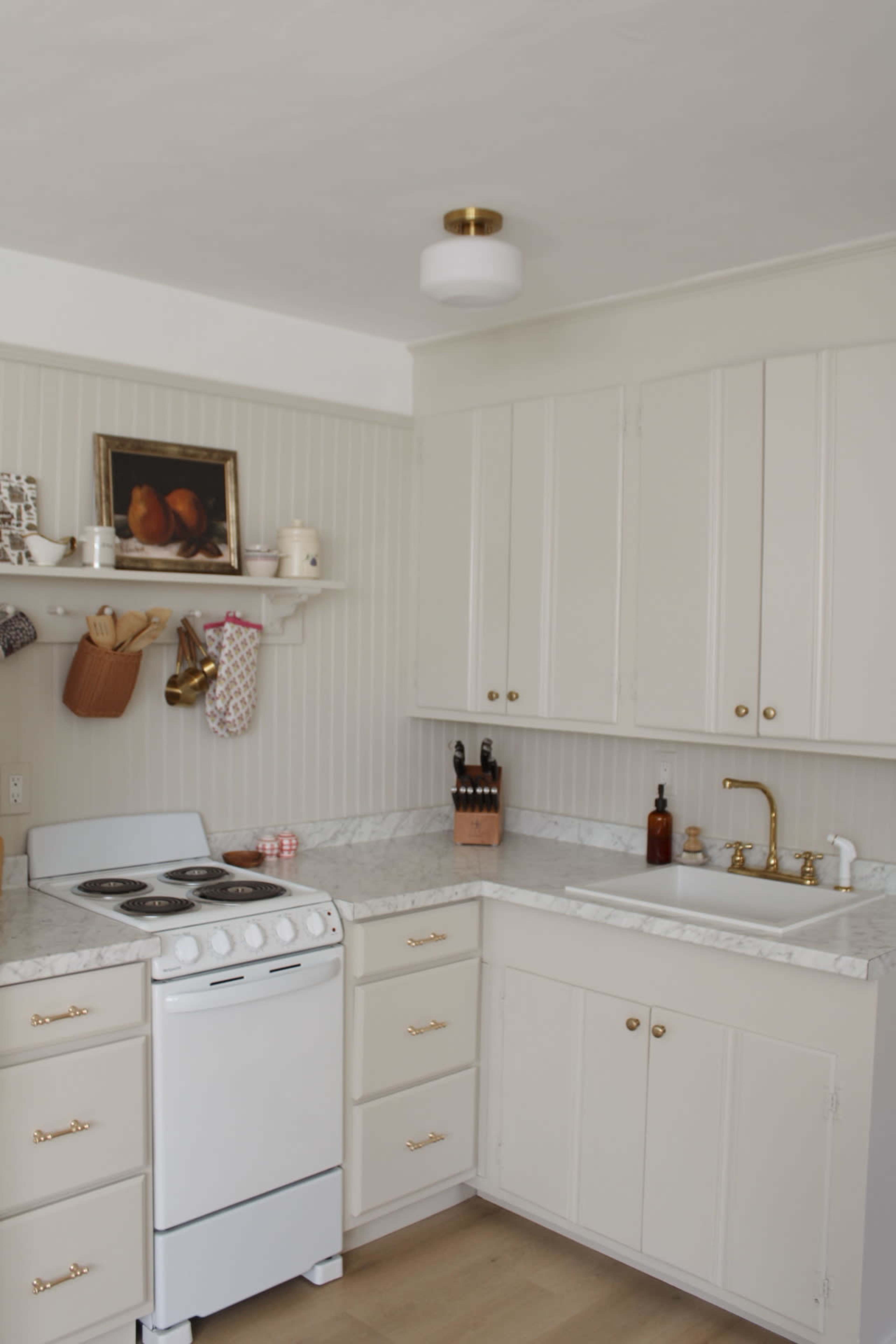 The image shows a modern kitchen with white cabinetry, a marble countertop, a stove, and a double basin sink.