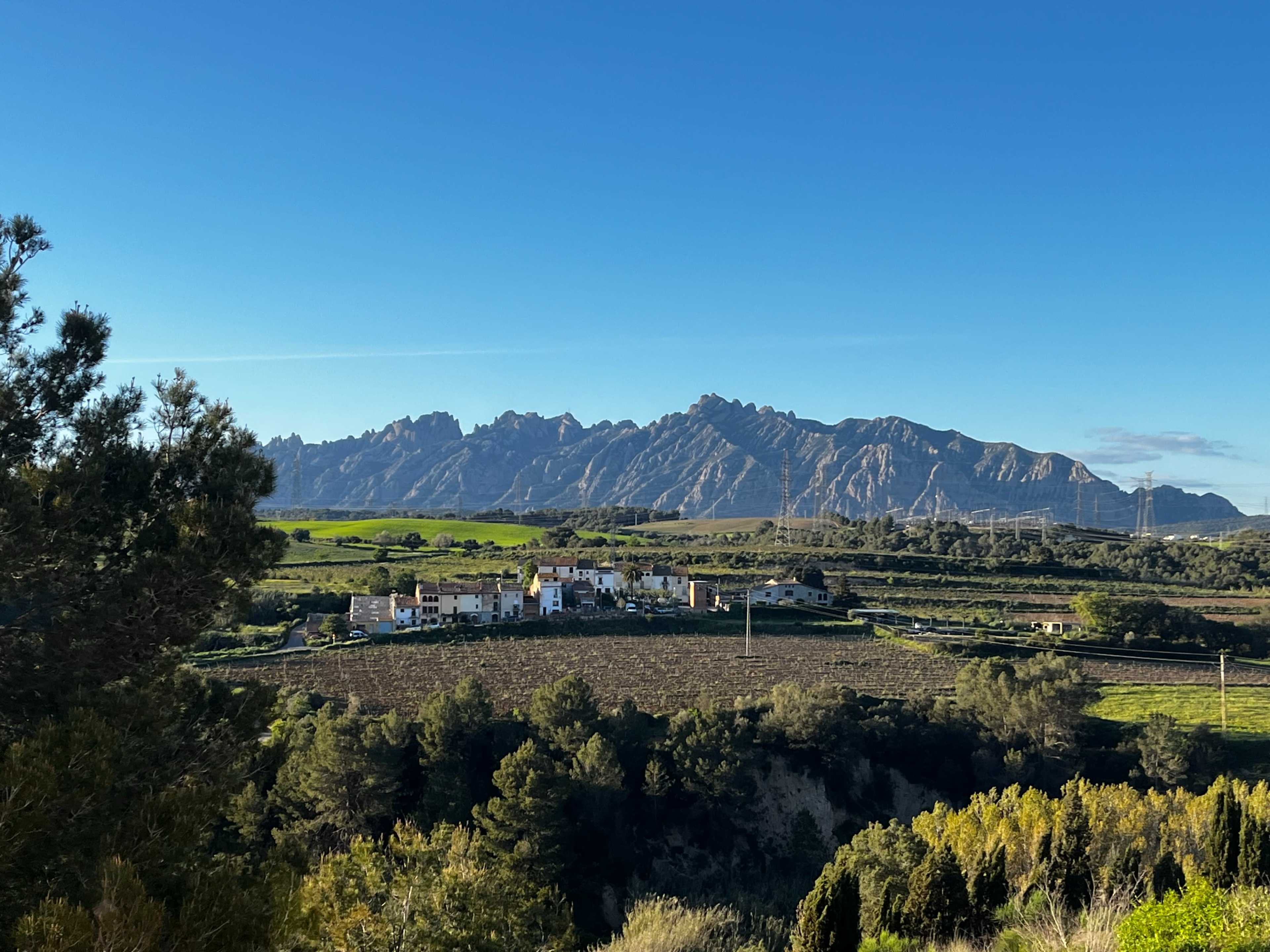 A village is nestled in a valley with mountains rising in the background under a clear blue sky.