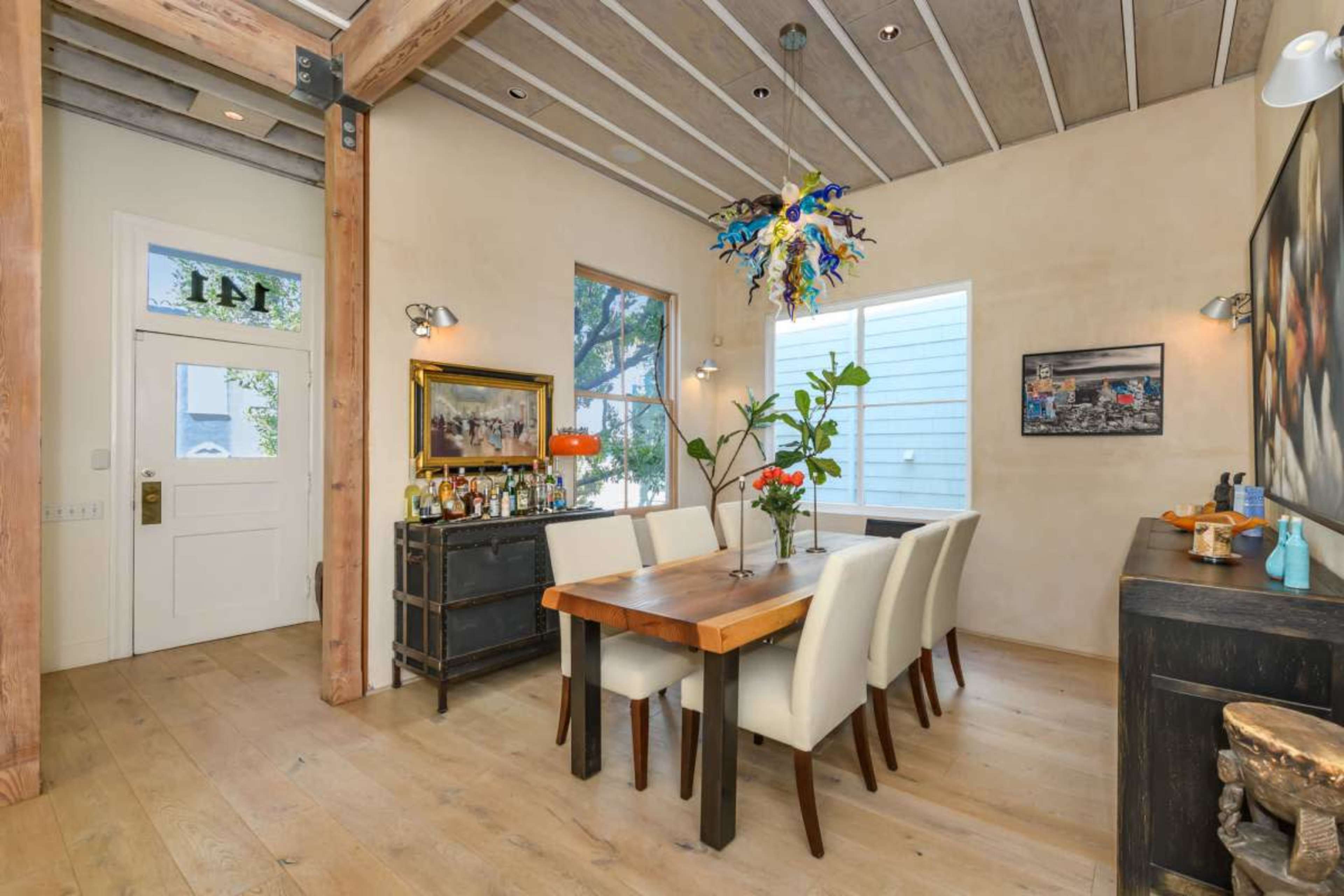 The image shows a dining area with a wooden table surrounded by white upholstered chairs, with a sideboard and decorative wall art.