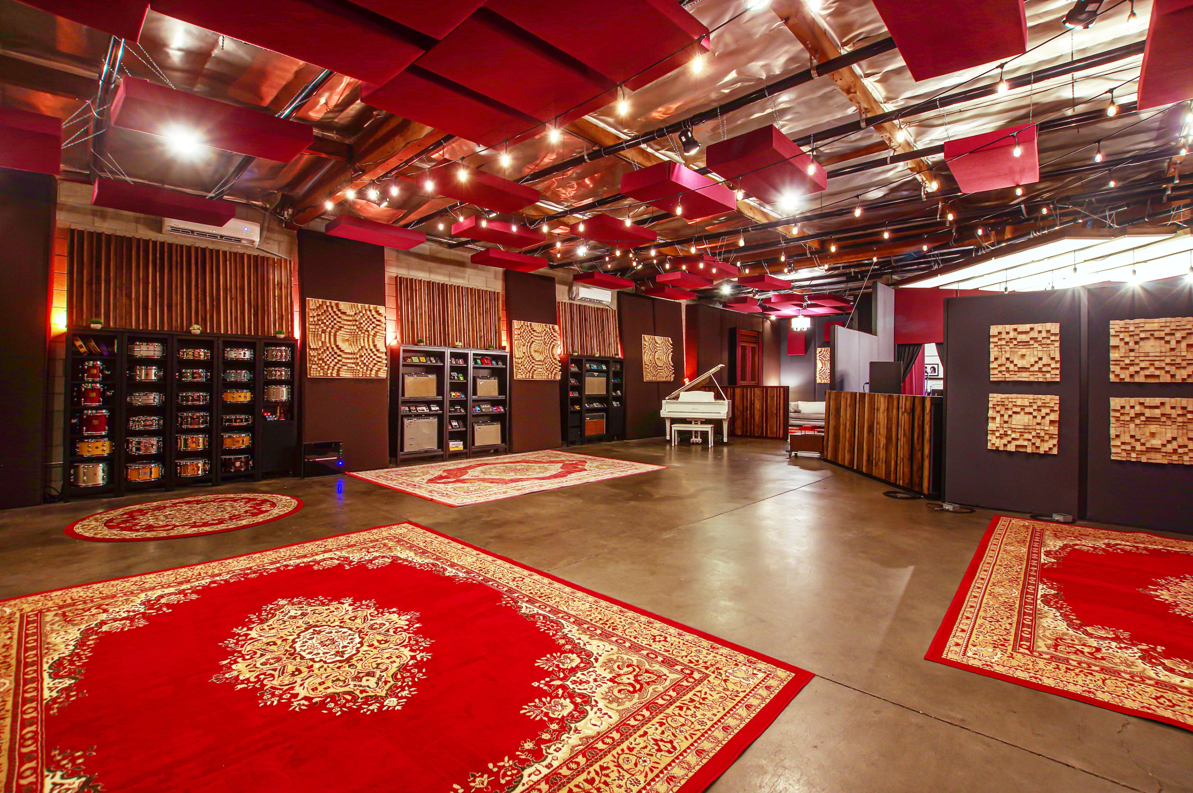 A spacious interior room designed for music or sound production, featuring red patterned rugs, dark walls, and acoustic panels on the ceiling.