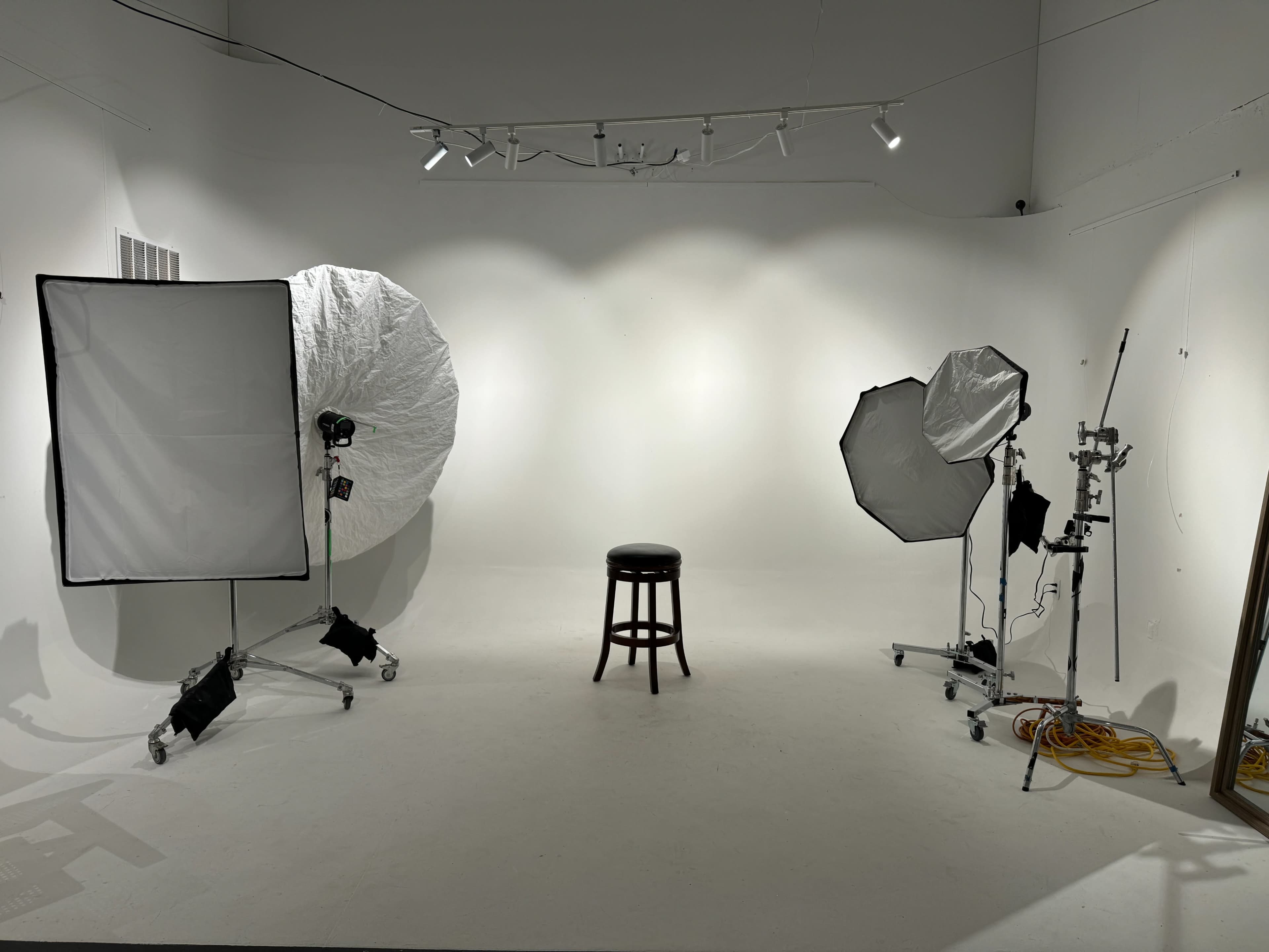 A photography studio is set up with two large light diffusers and a black stool positioned in the center on a white floor.