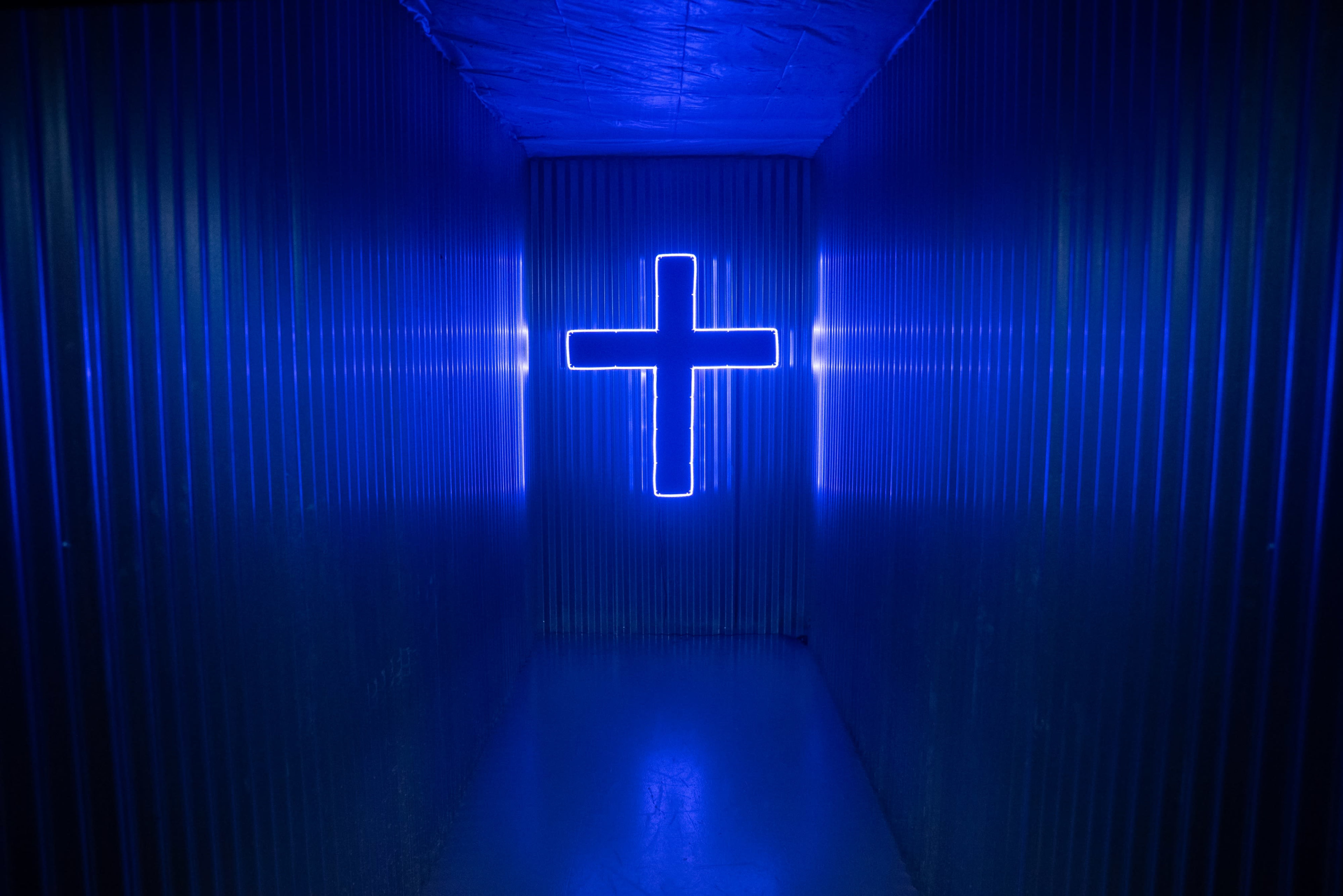 A blue-lit corridor features a large neon cross at the far end.
