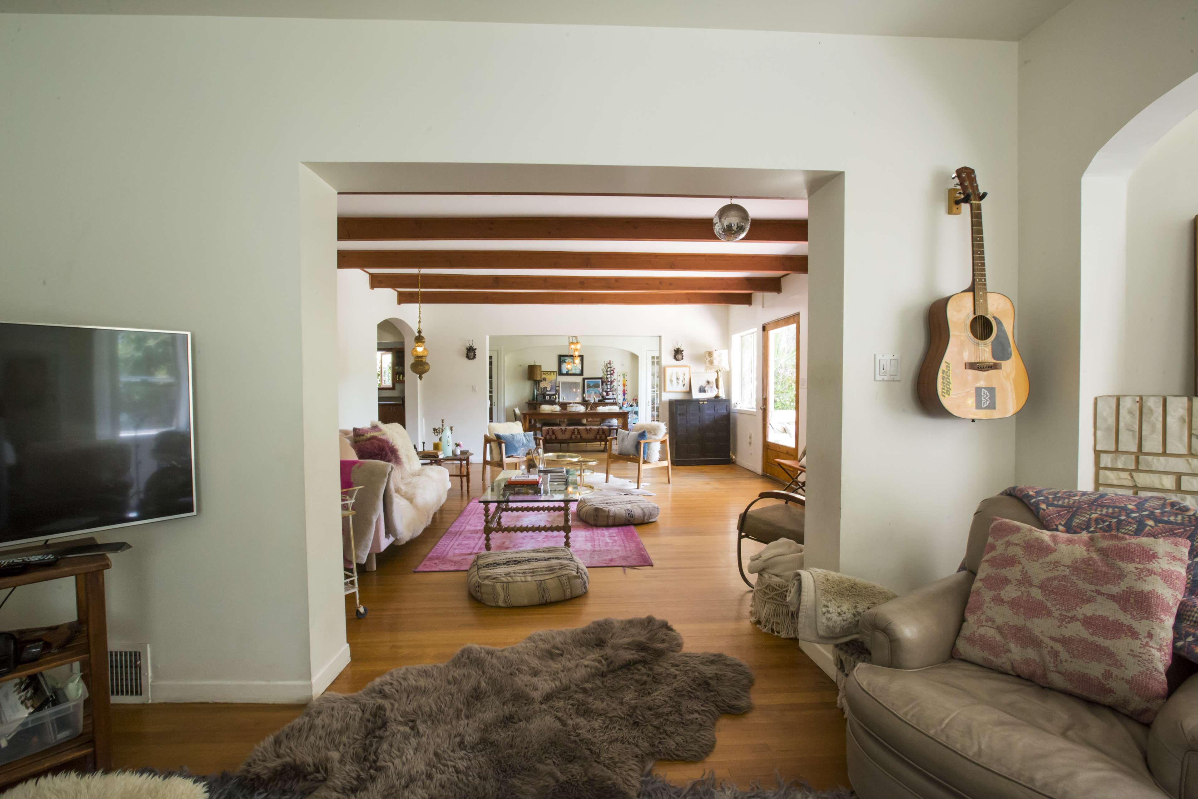 A living room with wooden beams, a central seating area, and a view into a dining area.