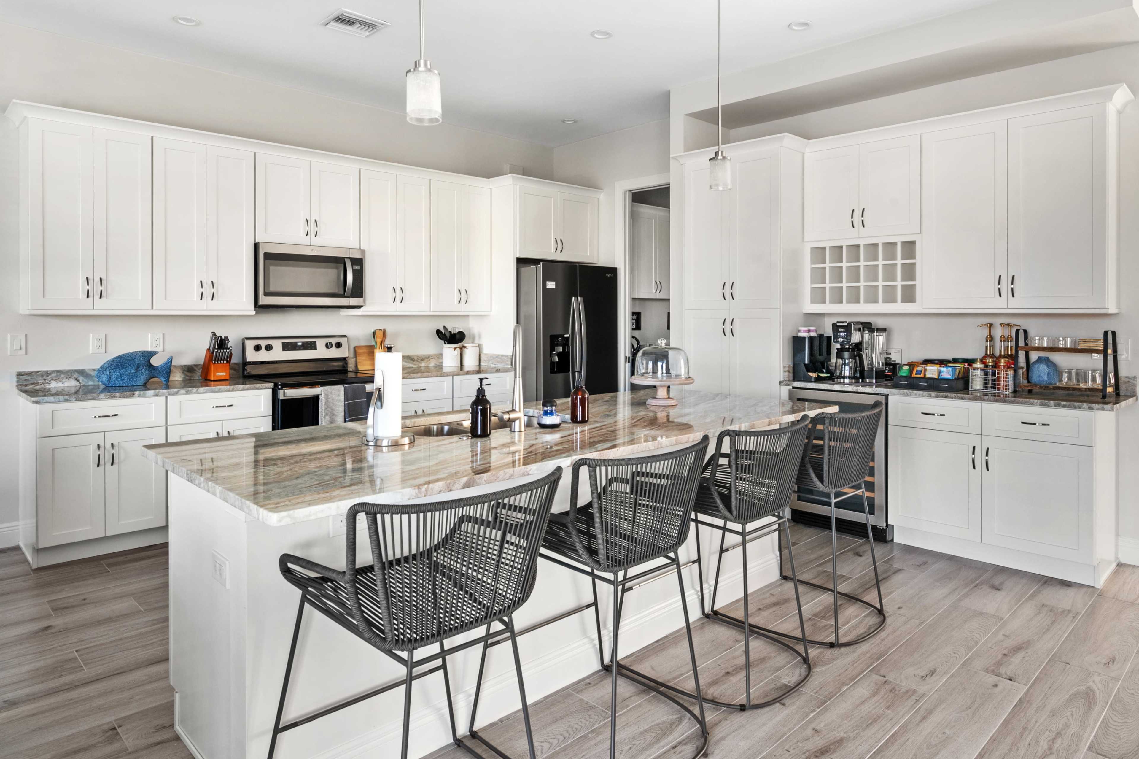 A modern kitchen features white cabinetry, stainless steel appliances, a large island with bar seating, and a light-colored wooden floor.