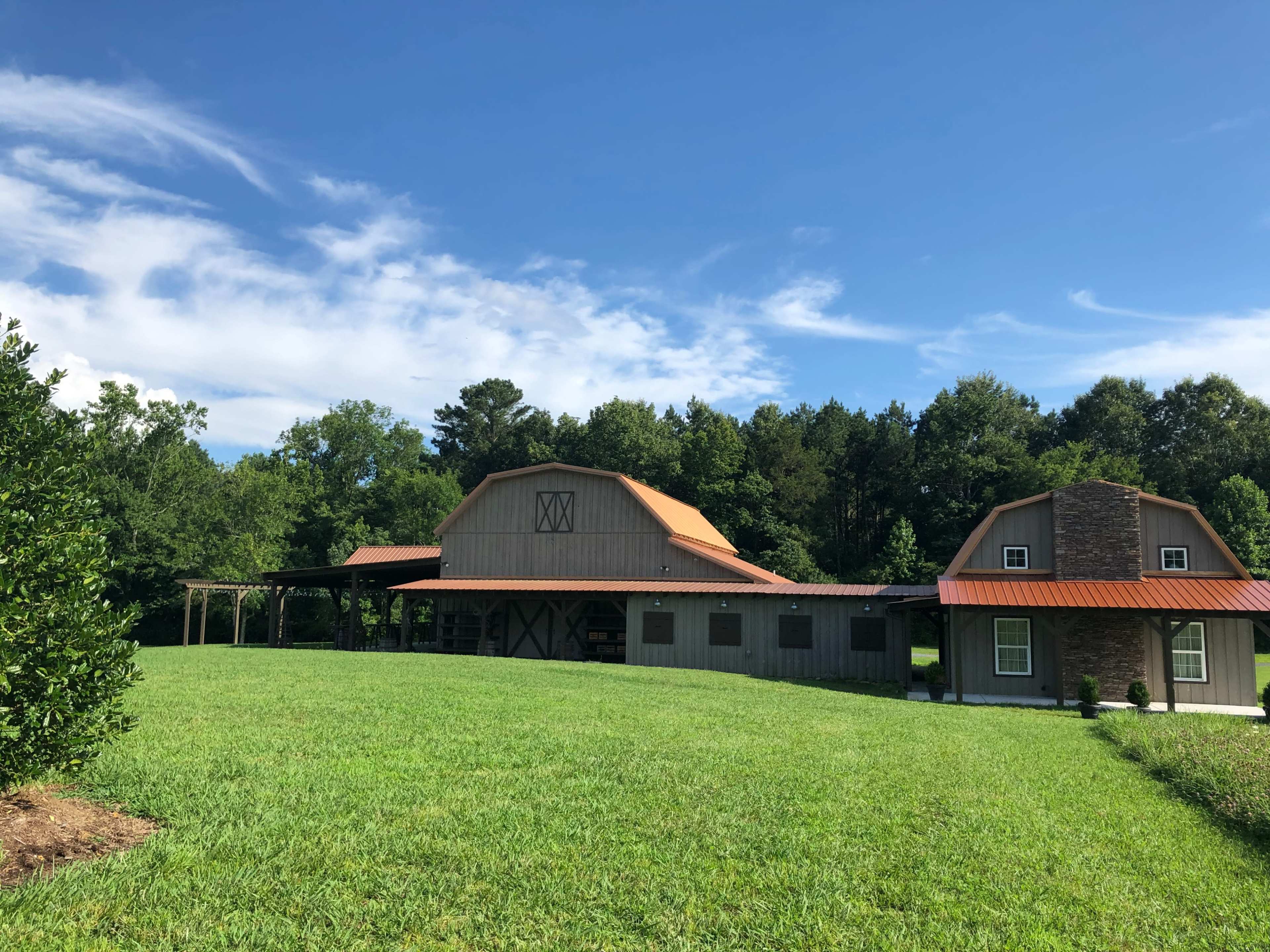 A large barn-style building with a red roof, set on a grassy lawn surrounded by trees under a blue sky.