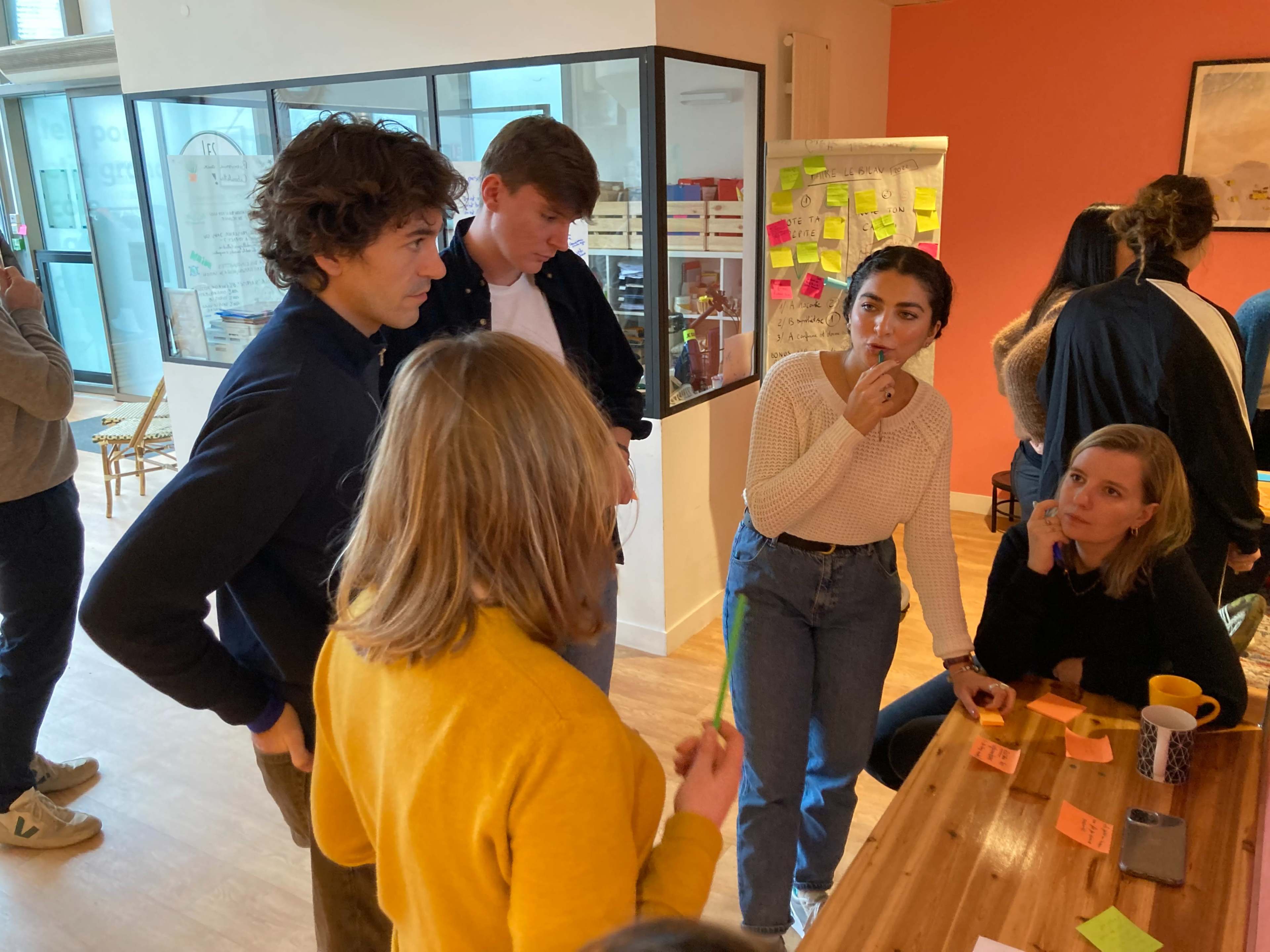 A group of young adults engages in a discussion around a table filled with sticky notes in a brightly lit workspace.