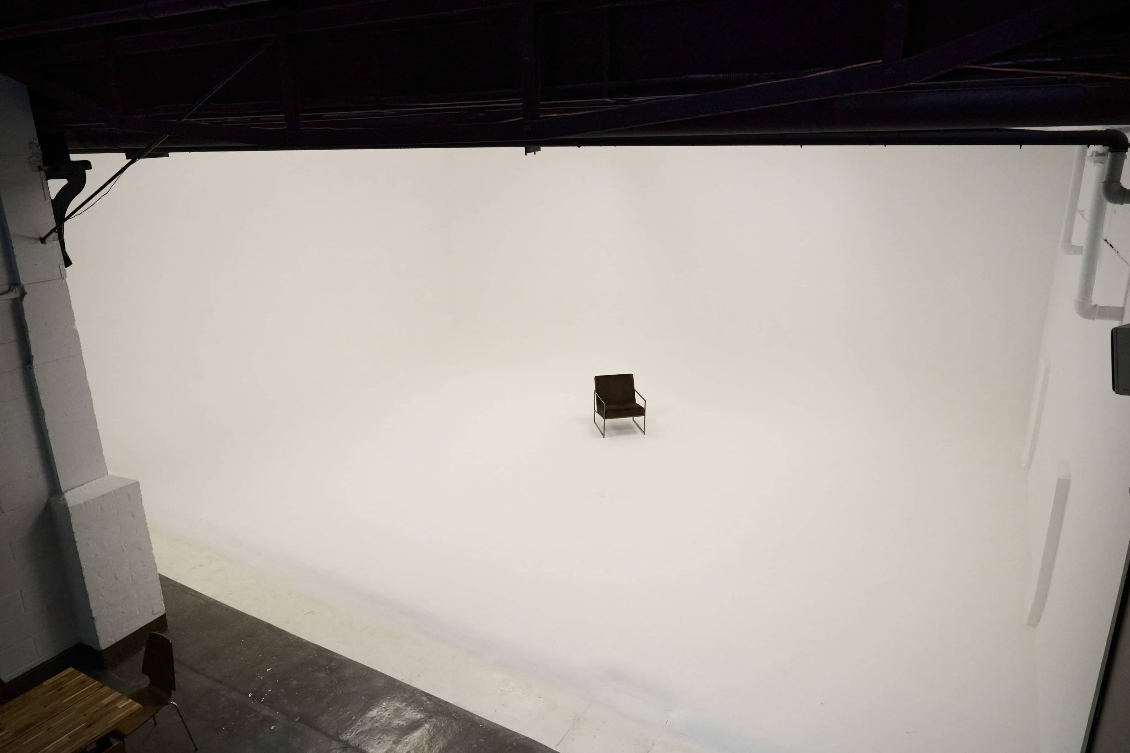 A single brown chair is centered in a spacious, empty white studio.