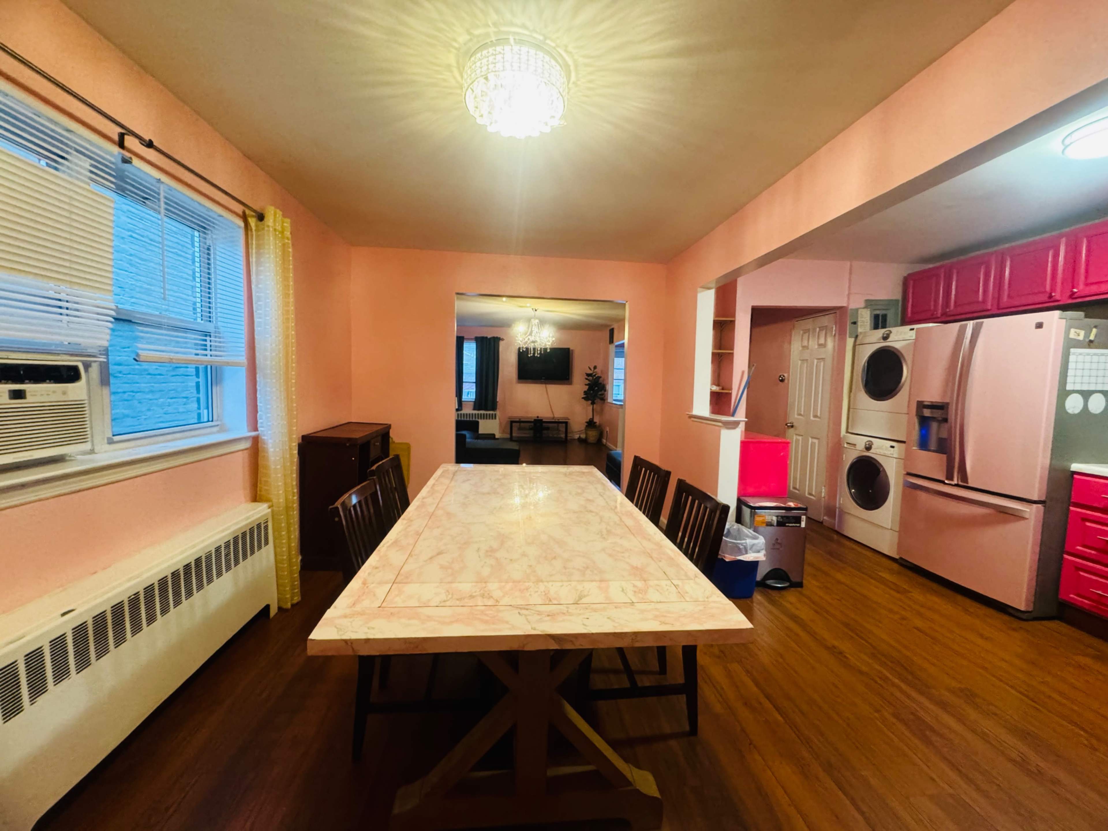 A dining area with a large marble table and wooden chairs, connected to a kitchen featuring pink cabinetry and appliances.
