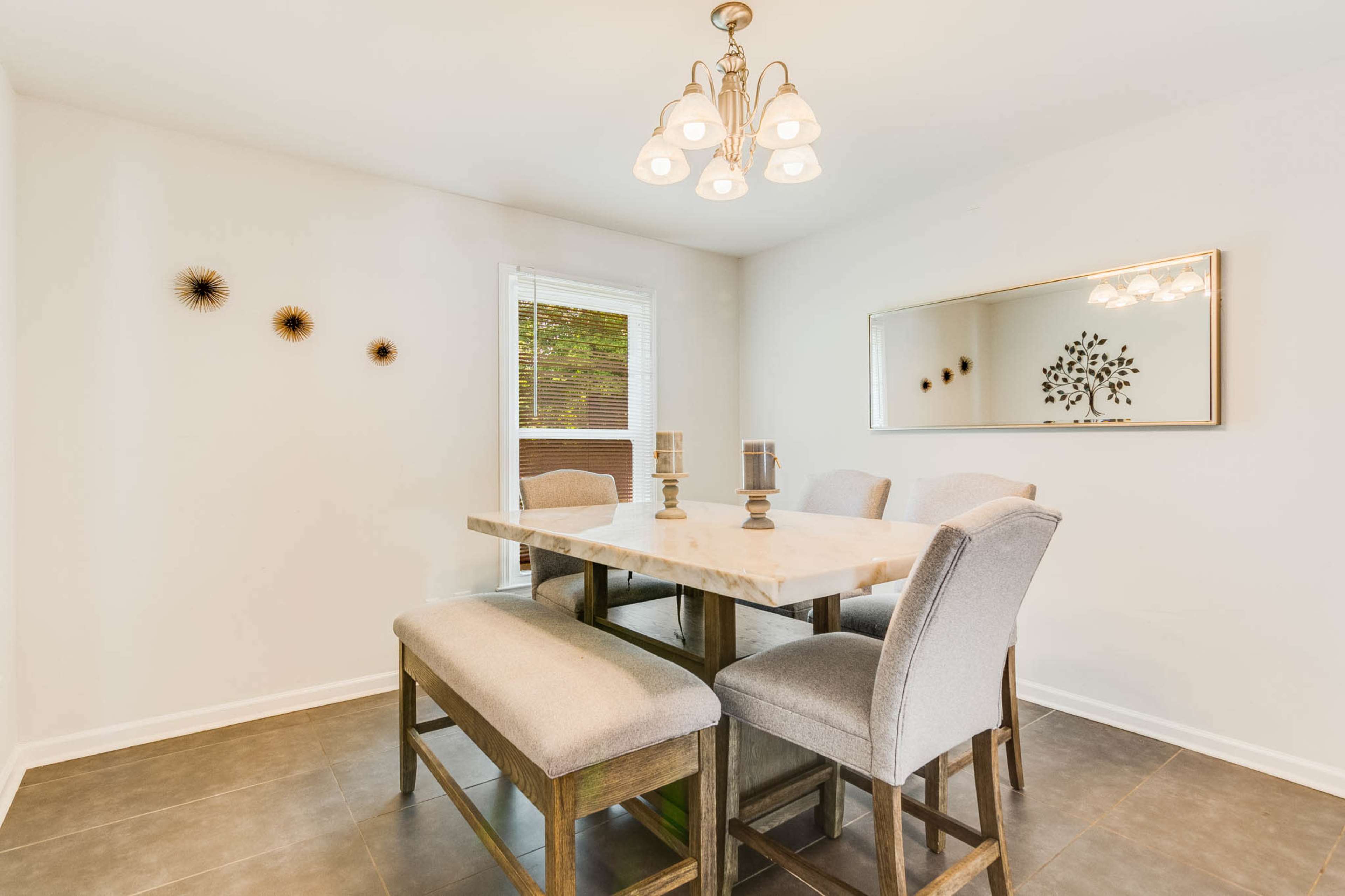 The image shows a modern dining area with a marble-top table surrounded by upholstered chairs and a bench, illuminated by a ceiling light fixture.