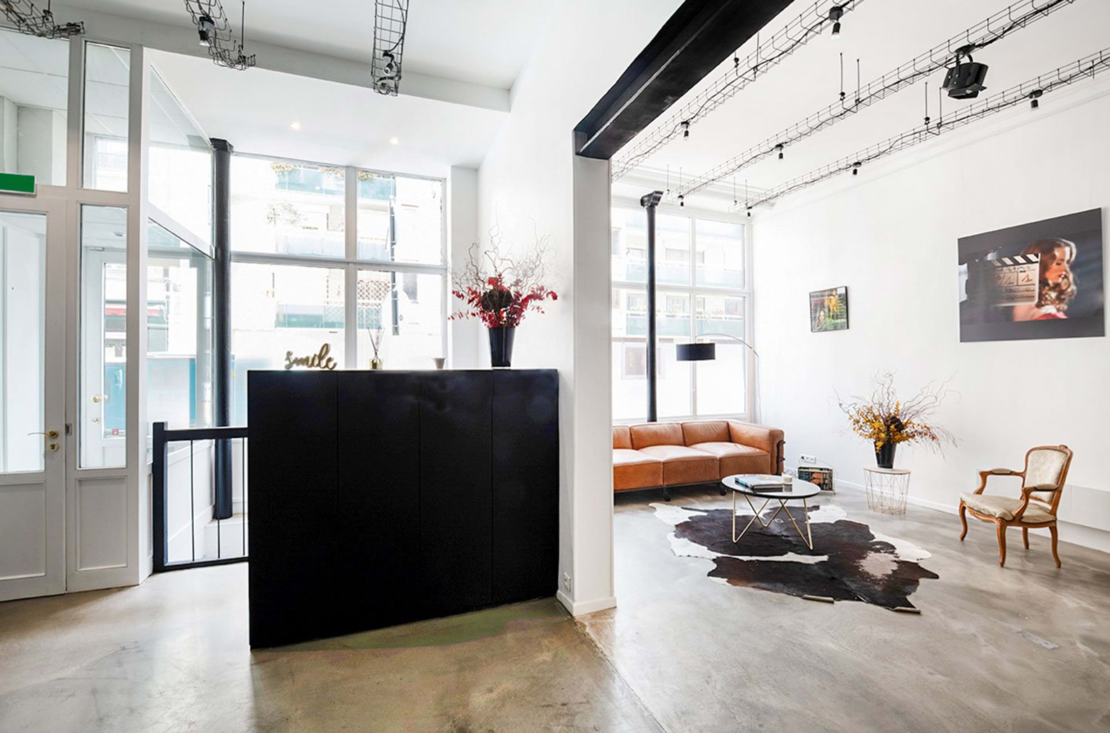 A modern interior space featuring a reception area with a black counter, a brown sofa, a coffee table on a cowhide rug, and large windows letting in natural light.