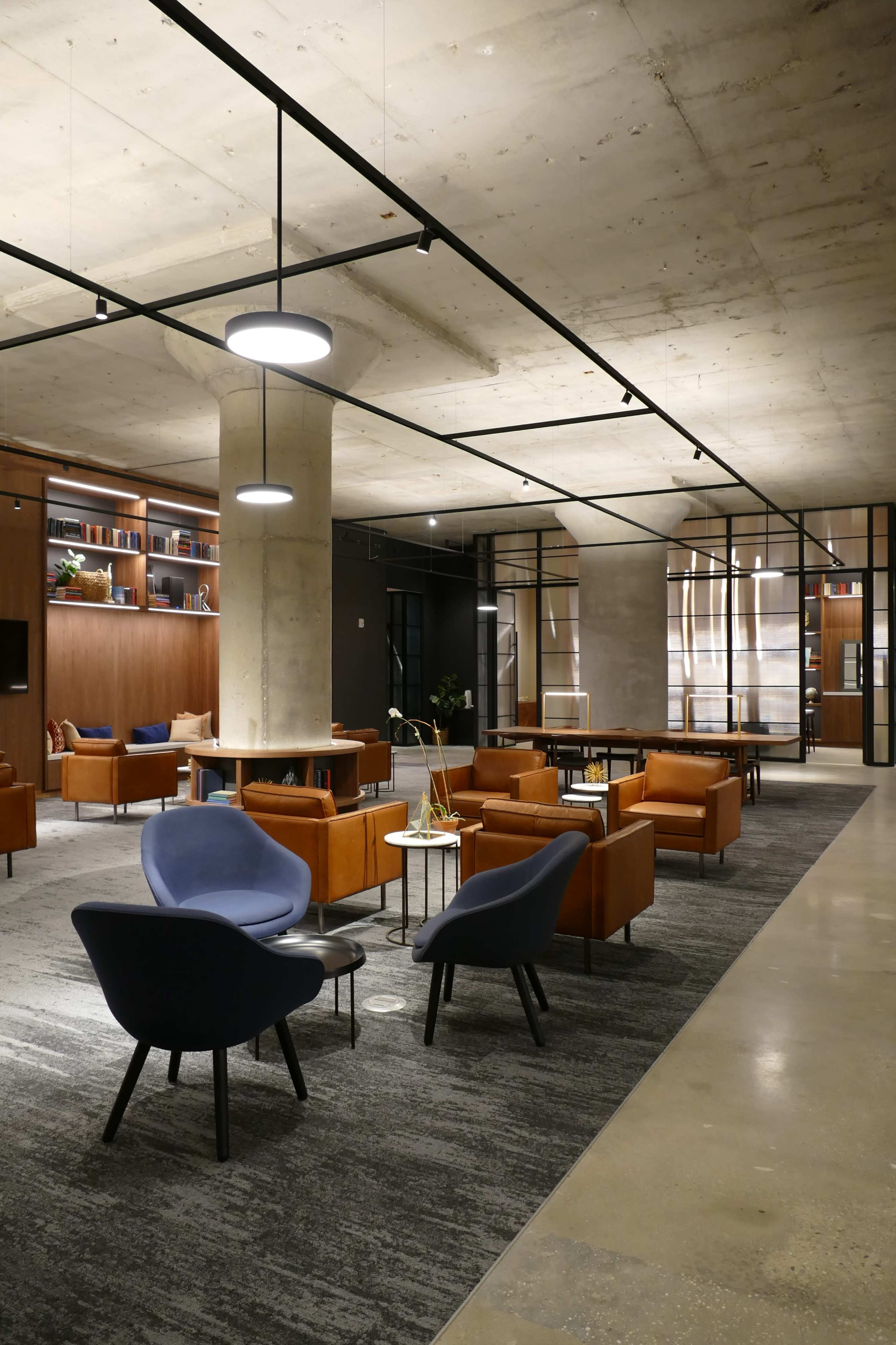 A modern lounge area with a mix of orange and blue chairs, a coffee table, and shelves in the background against a concrete wall.