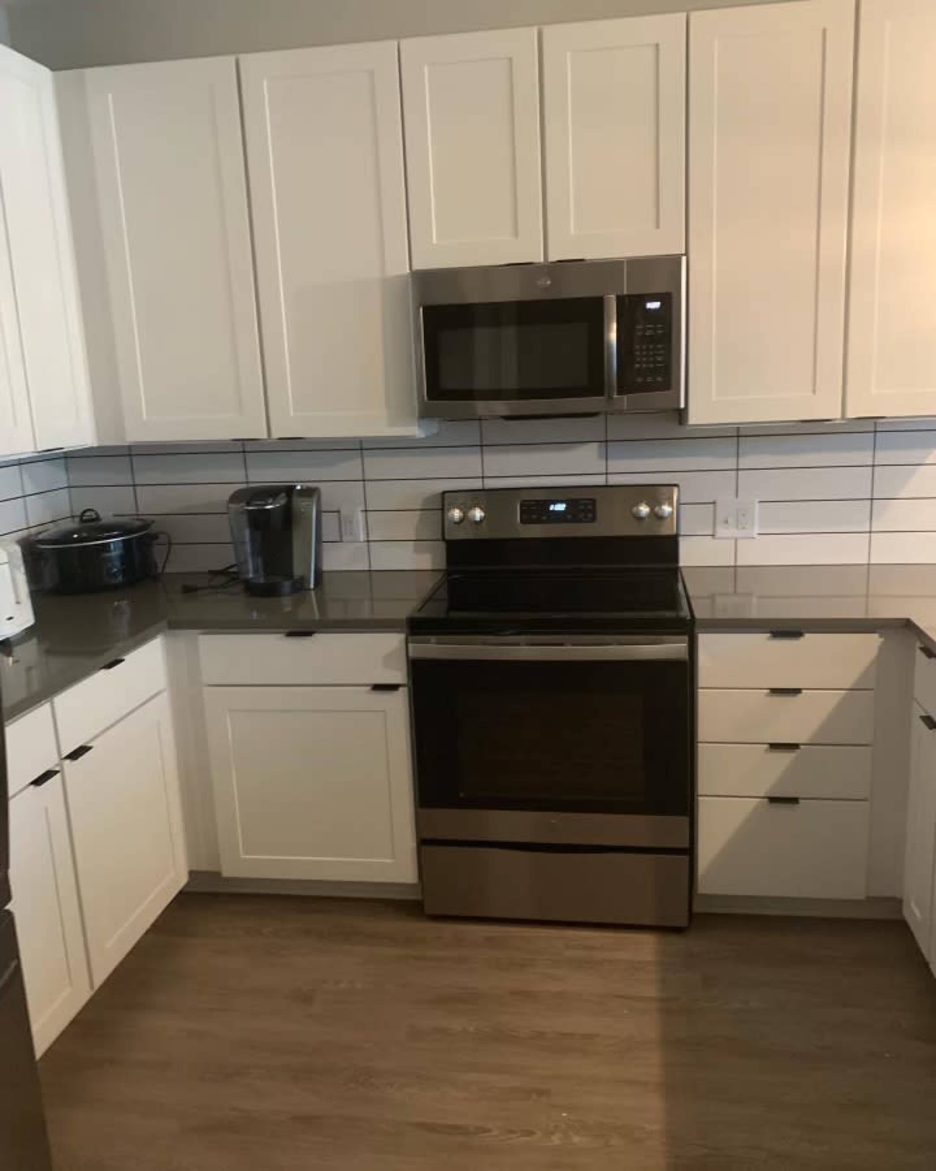 A modern kitchen with white cabinets, a stainless steel stove, microwave, and a countertop with a coffee maker and a pot.