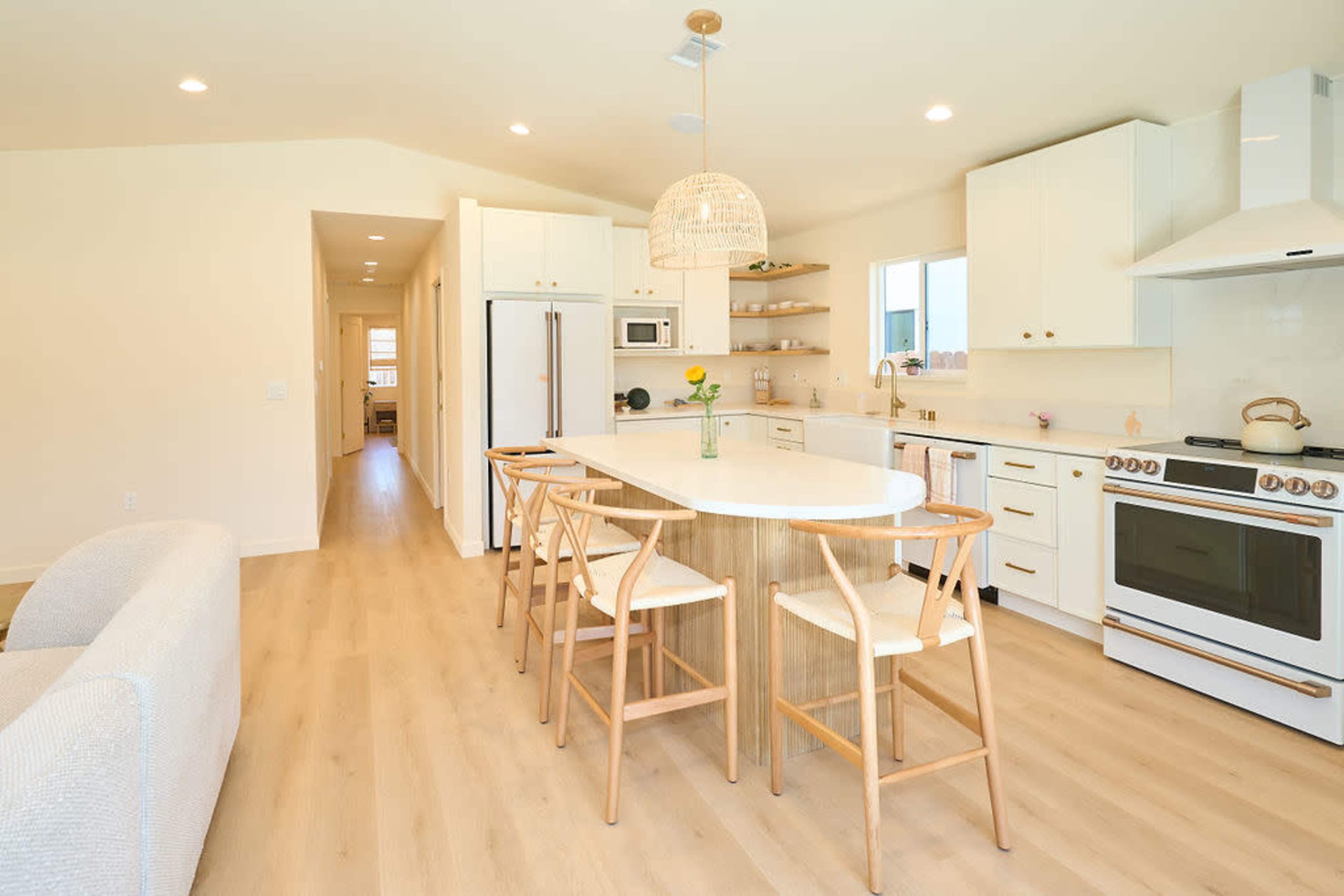 A modern kitchen features white cabinetry, a large island with bar stools, and an adjacent hallway leading to other rooms.