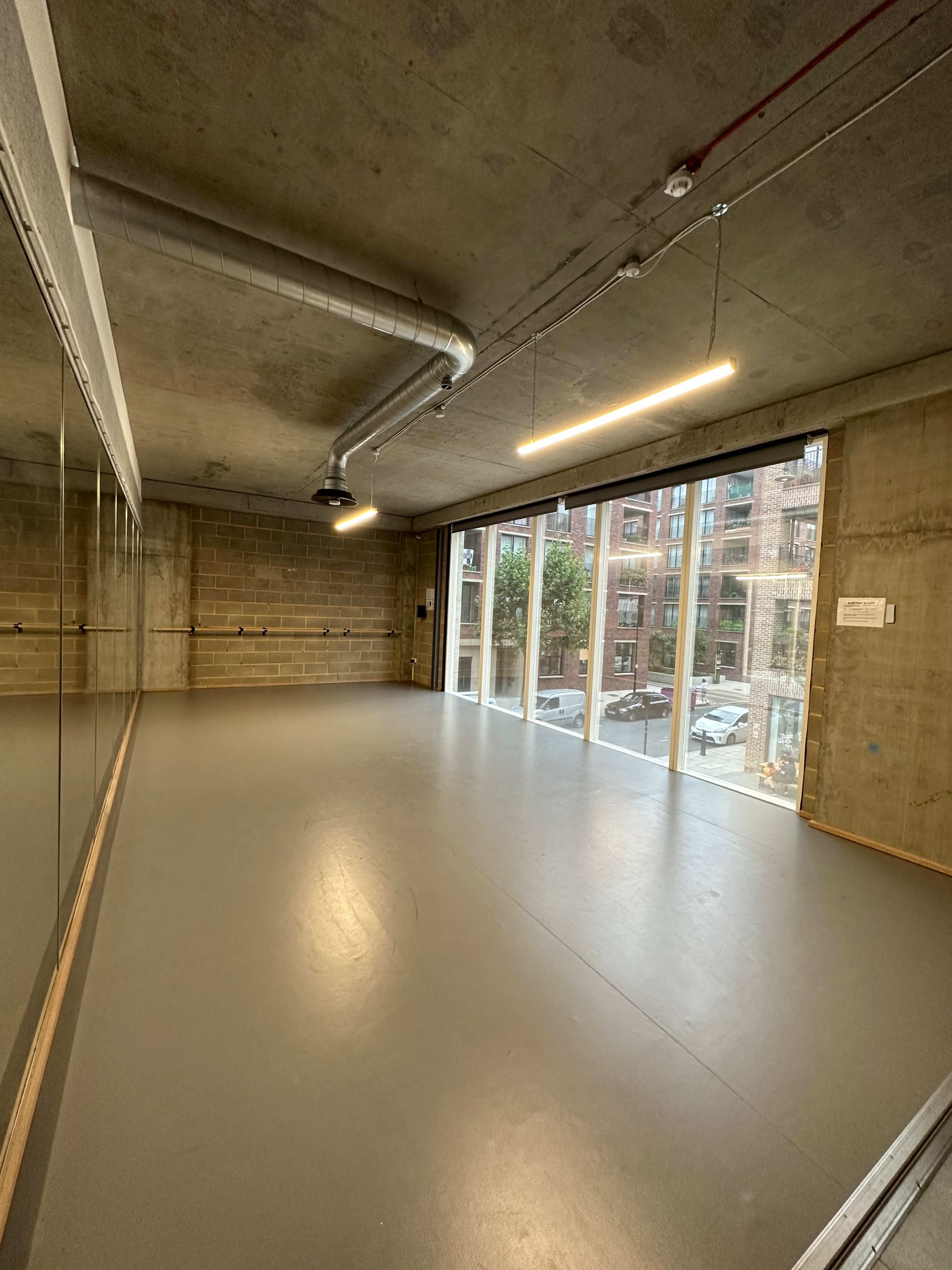 A spacious dance studio with large windows and a concrete ceiling.