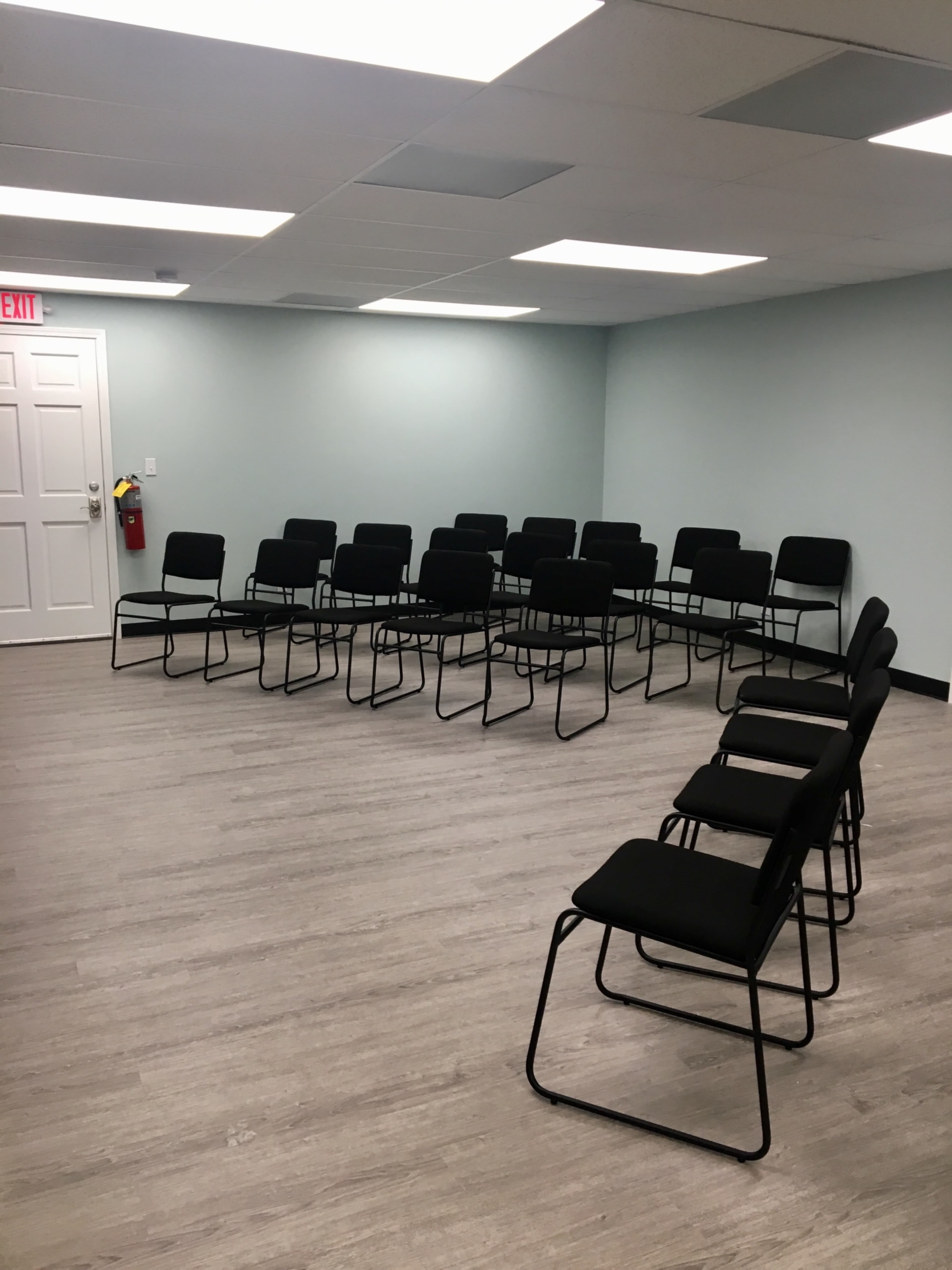 A room with a circle of black chairs arranged on a light-colored wooden floor.