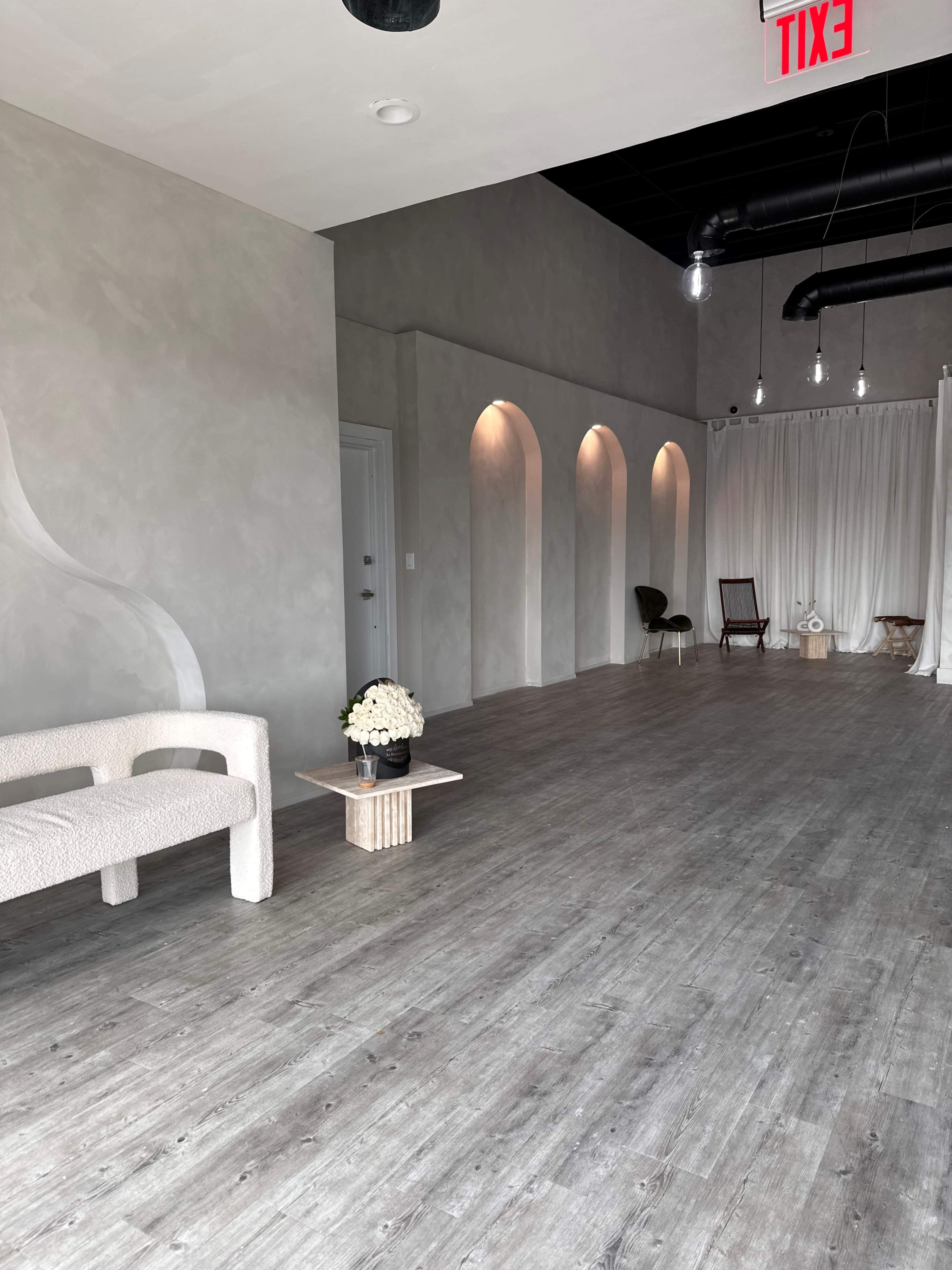 A minimalist interior space with arched alcoves, a light-colored sofa, and wooden flooring, accentuated by simple decor items.