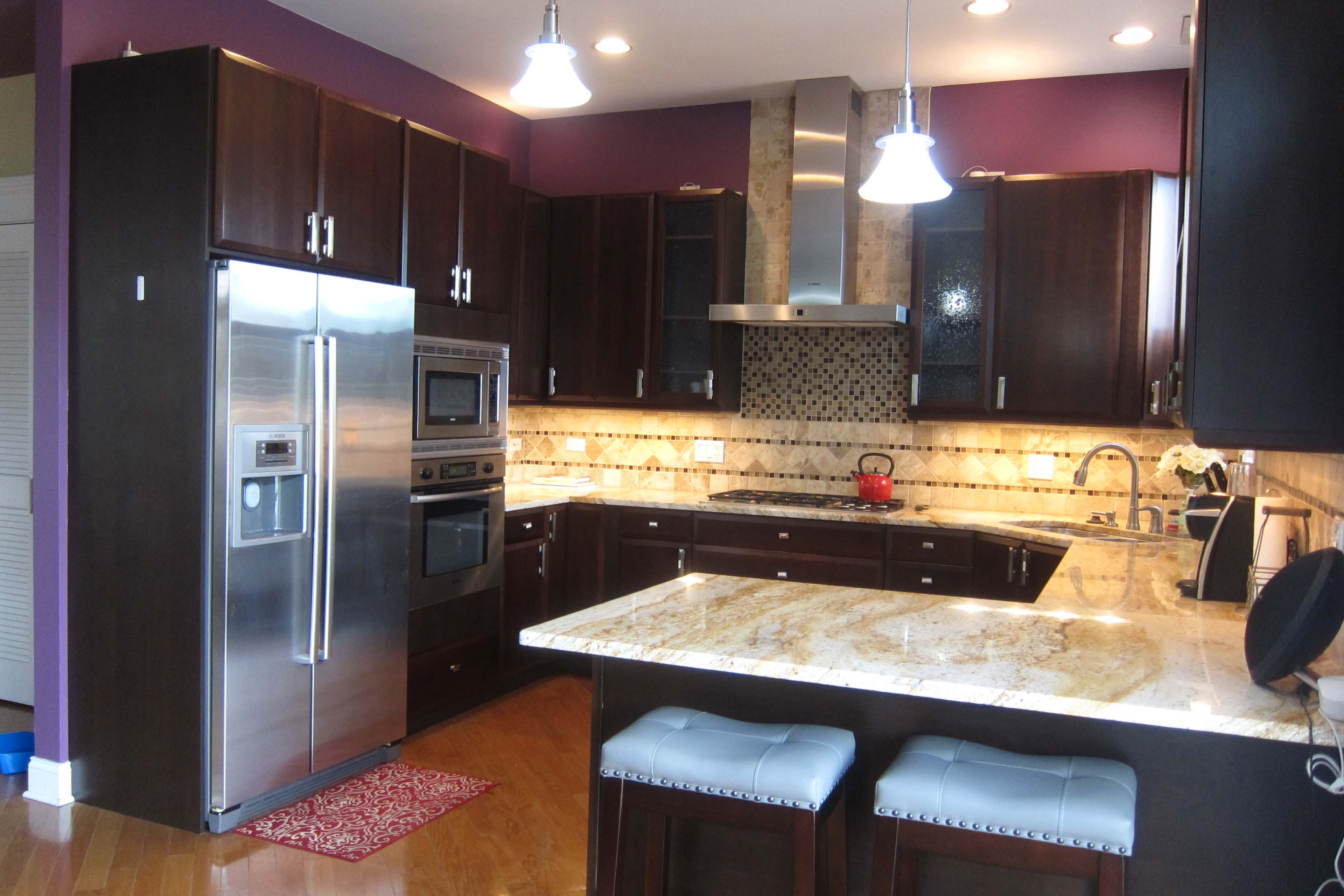 The kitchen features dark wooden cabinets, stainless steel appliances, and a granite countertop with a central island and bar seating.