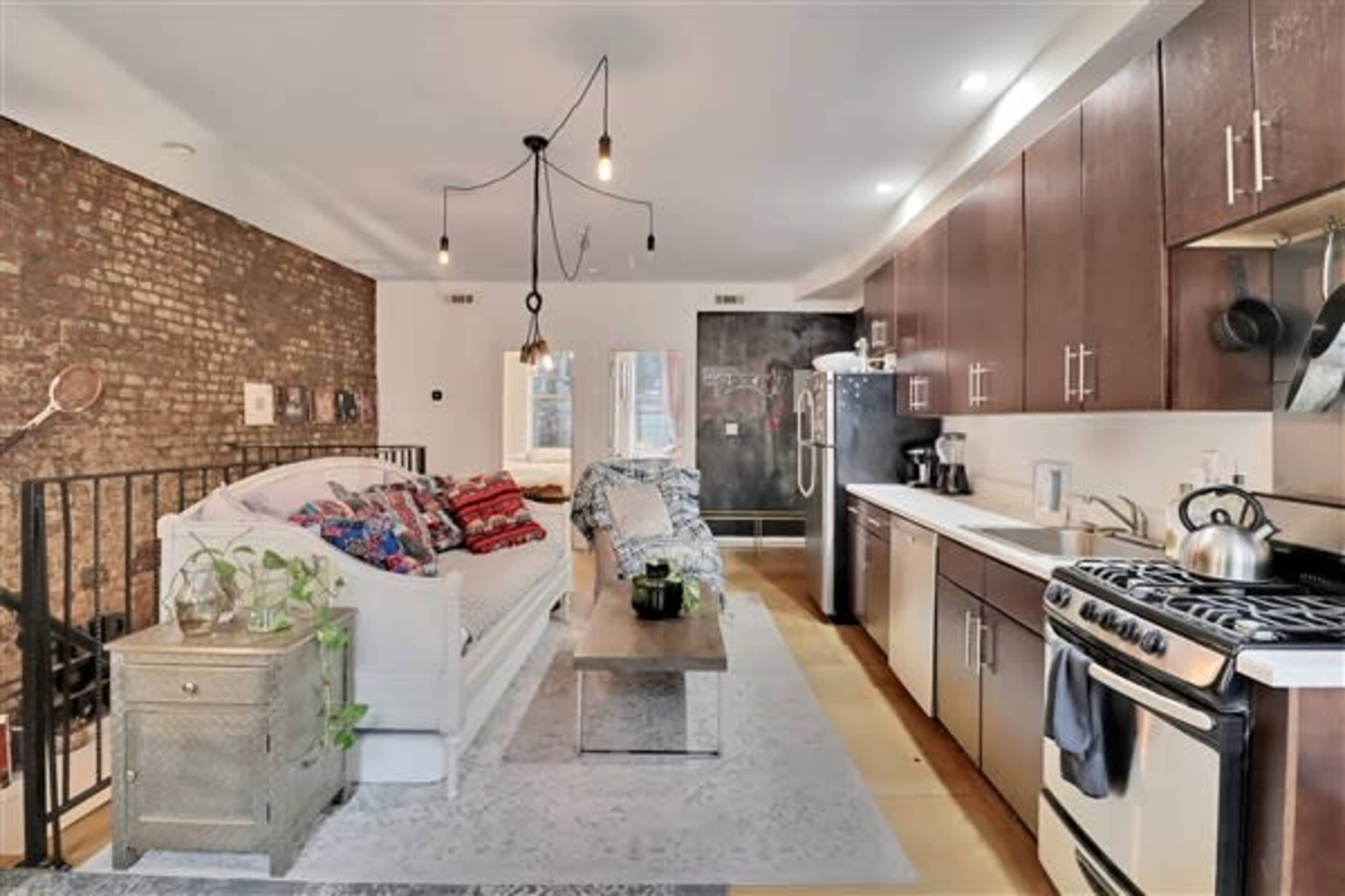 A modern kitchen and living area featuring a sofa with colorful cushions, a coffee table, and a brick accent wall.