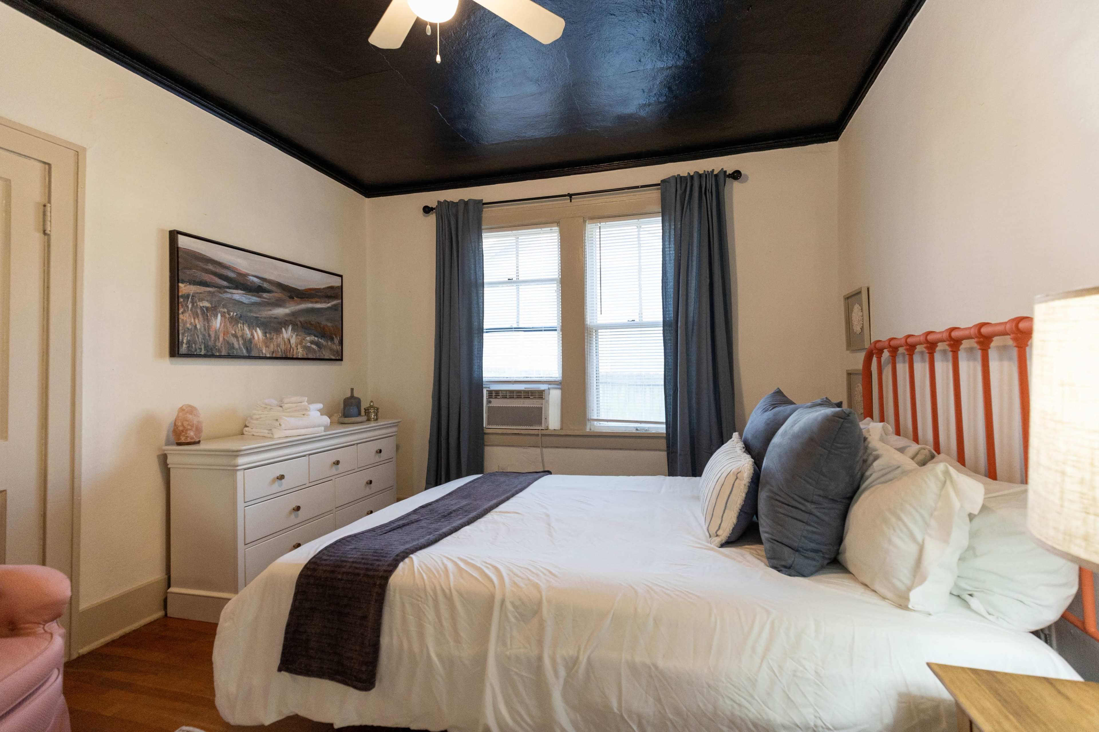 A neatly arranged bedroom features a bed with decorative pillows, a dresser, and an air conditioning unit by the window.